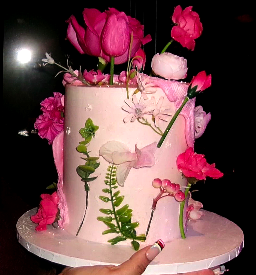 A pink and white cake decorated with various pink flowers and green leaves.