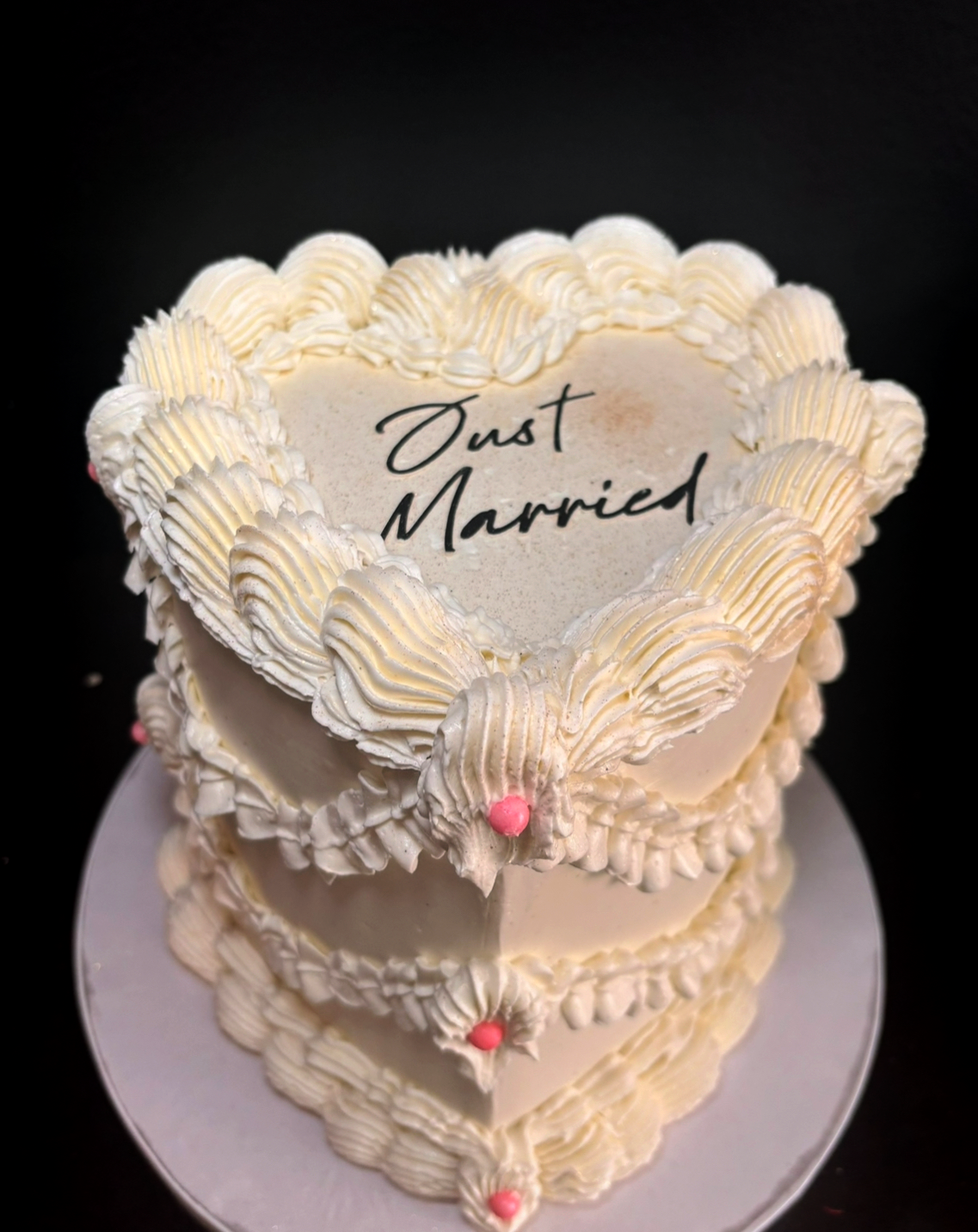A tiered wedding cake decorated with white frosting and pink pearls, with the message "Just Married" written on top.