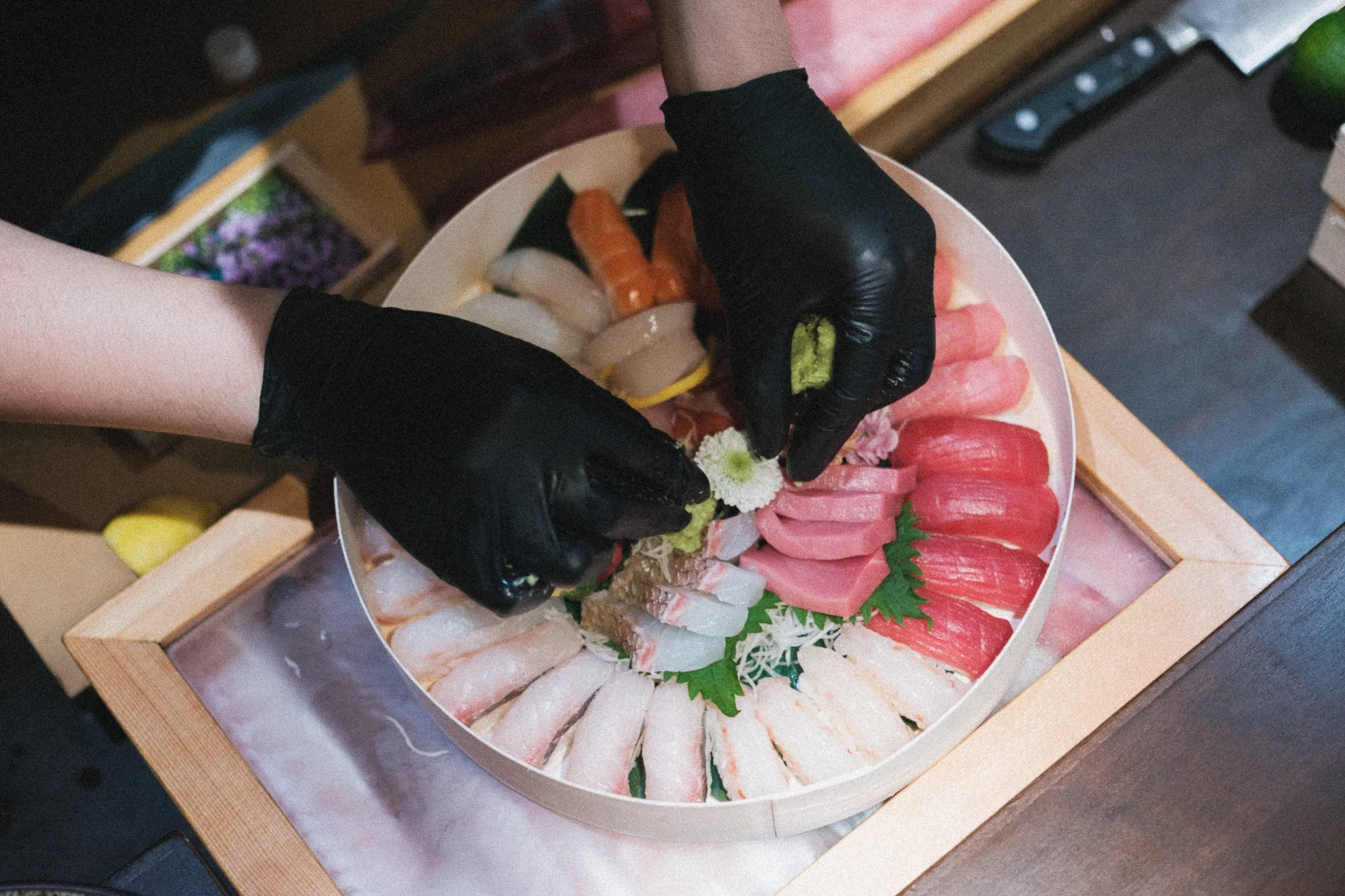 A chef arranging a platter of assorted sashimi and sushi on a wooden table.