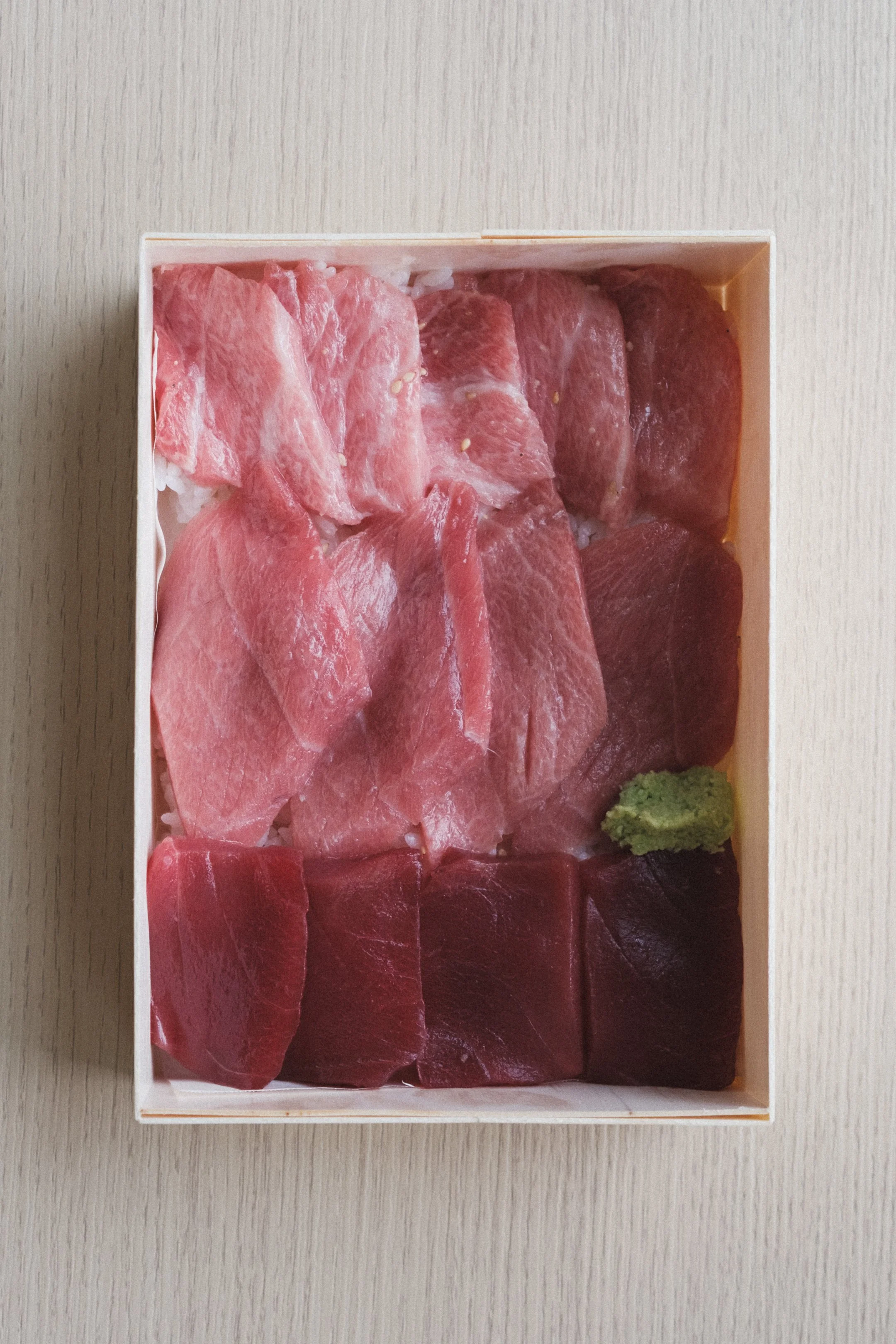 A rectangular box of assorted raw bluefin tuna sashimi with wasabi on the side.