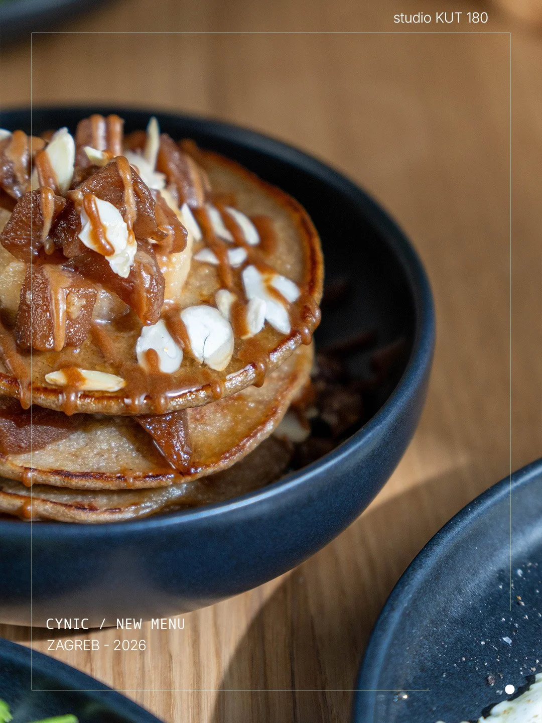 Stack of pancakes topped with caramel sauce, chopped nuts, and white chocolate shavings in a black bowl.