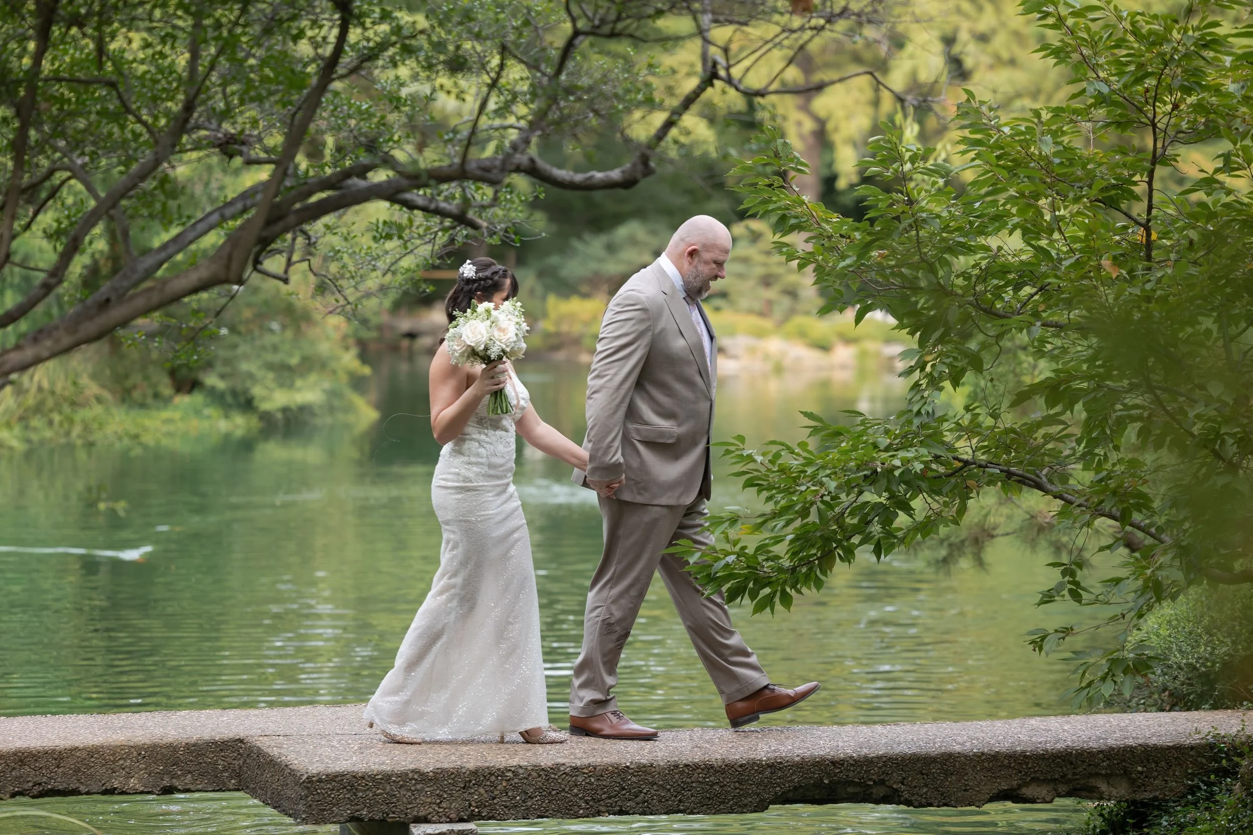 Lydia and Ryan walking hand in hand along the pond at the Fort Worth Japanese Garden