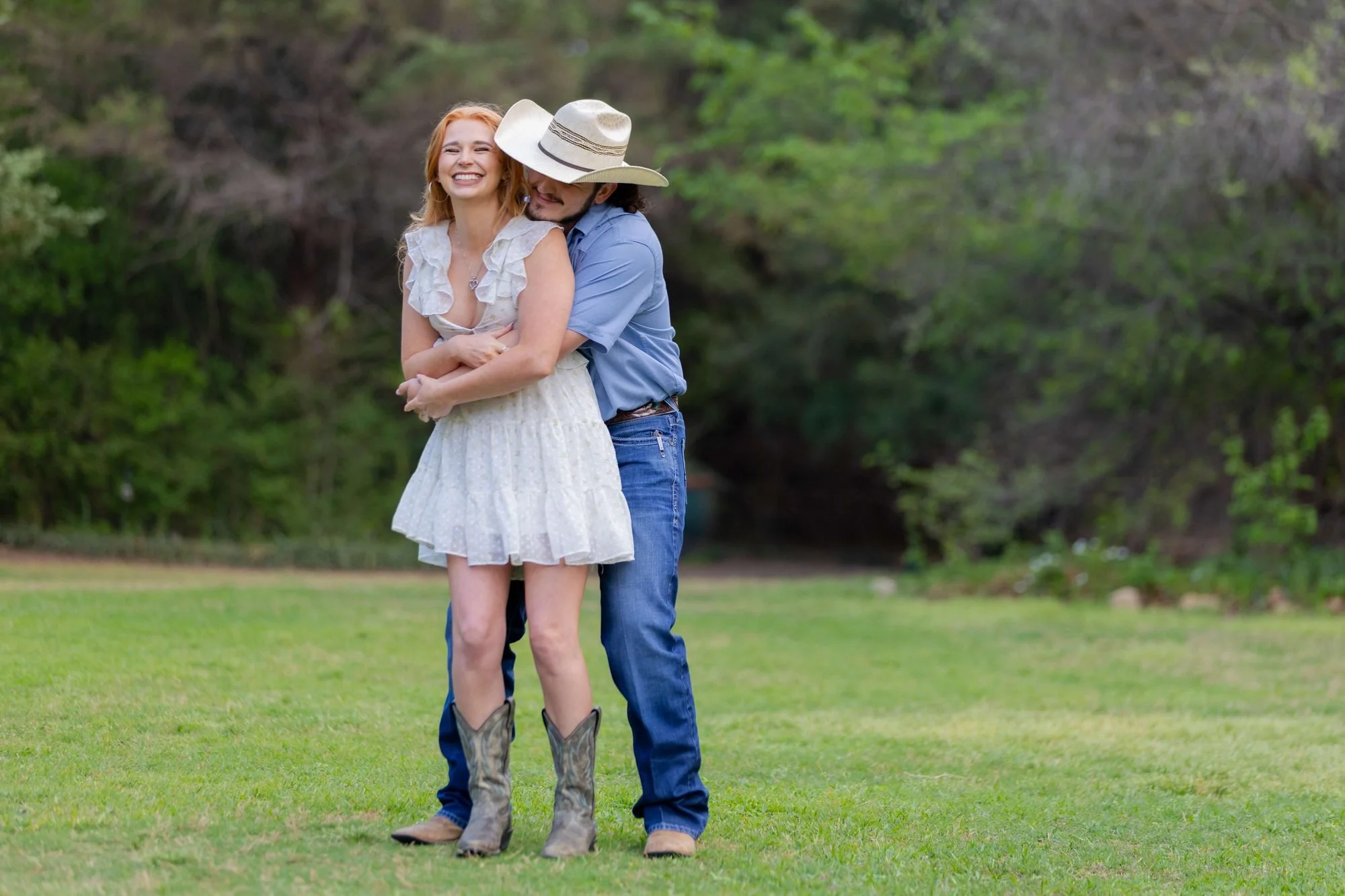 Playful DFW engagement photos of a couple hugging, him in a cowboy hat and her in cowboy boots