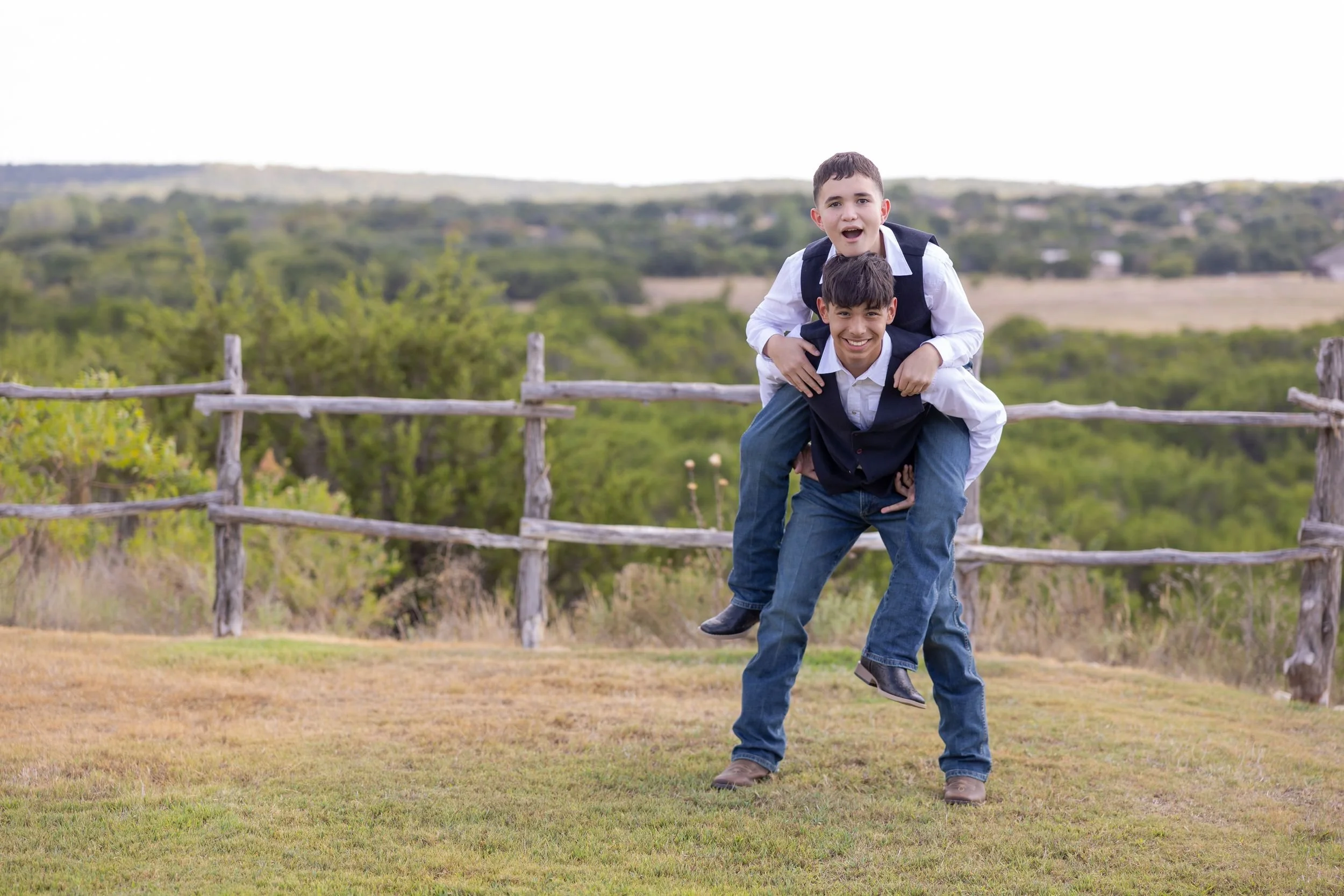 Playful groomsmen piggyback photo by the fence on the Dove Ridge Vineyard grounds