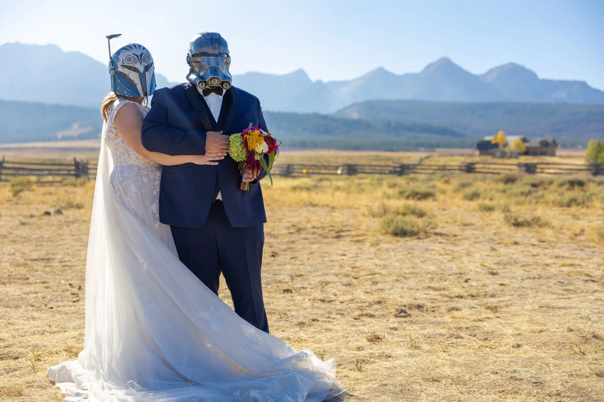 Bride and groom in Star Wars helmets posing in a field at a themed mountain wedding
