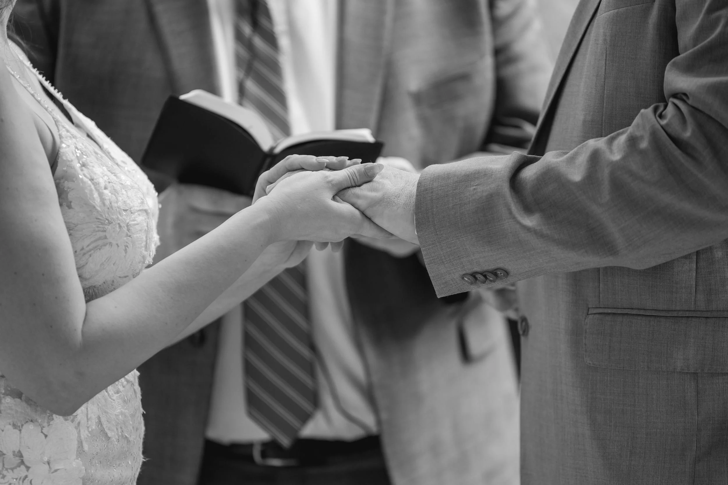 Black-and-white close-up of the bride and groom holding hands during their vows
