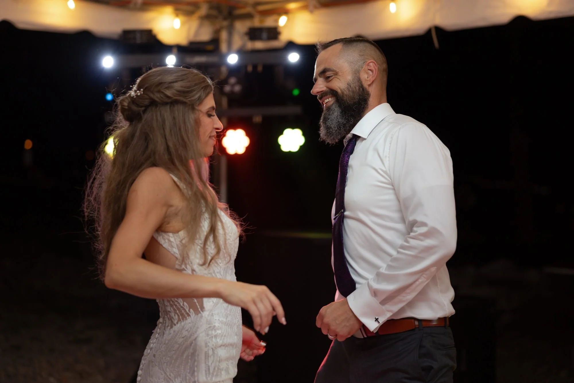 Bride and groom dancing under colorful string lights at their wedding reception