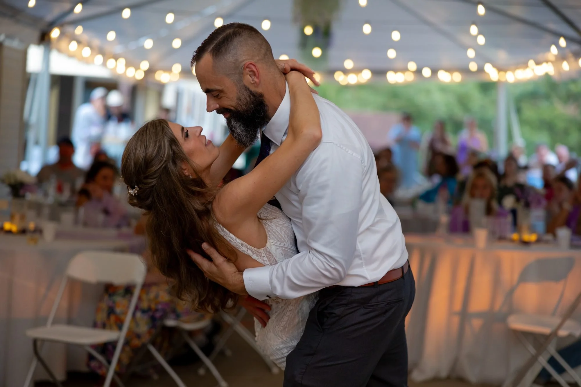 Groom dips the bride under string lights at a tent wedding reception