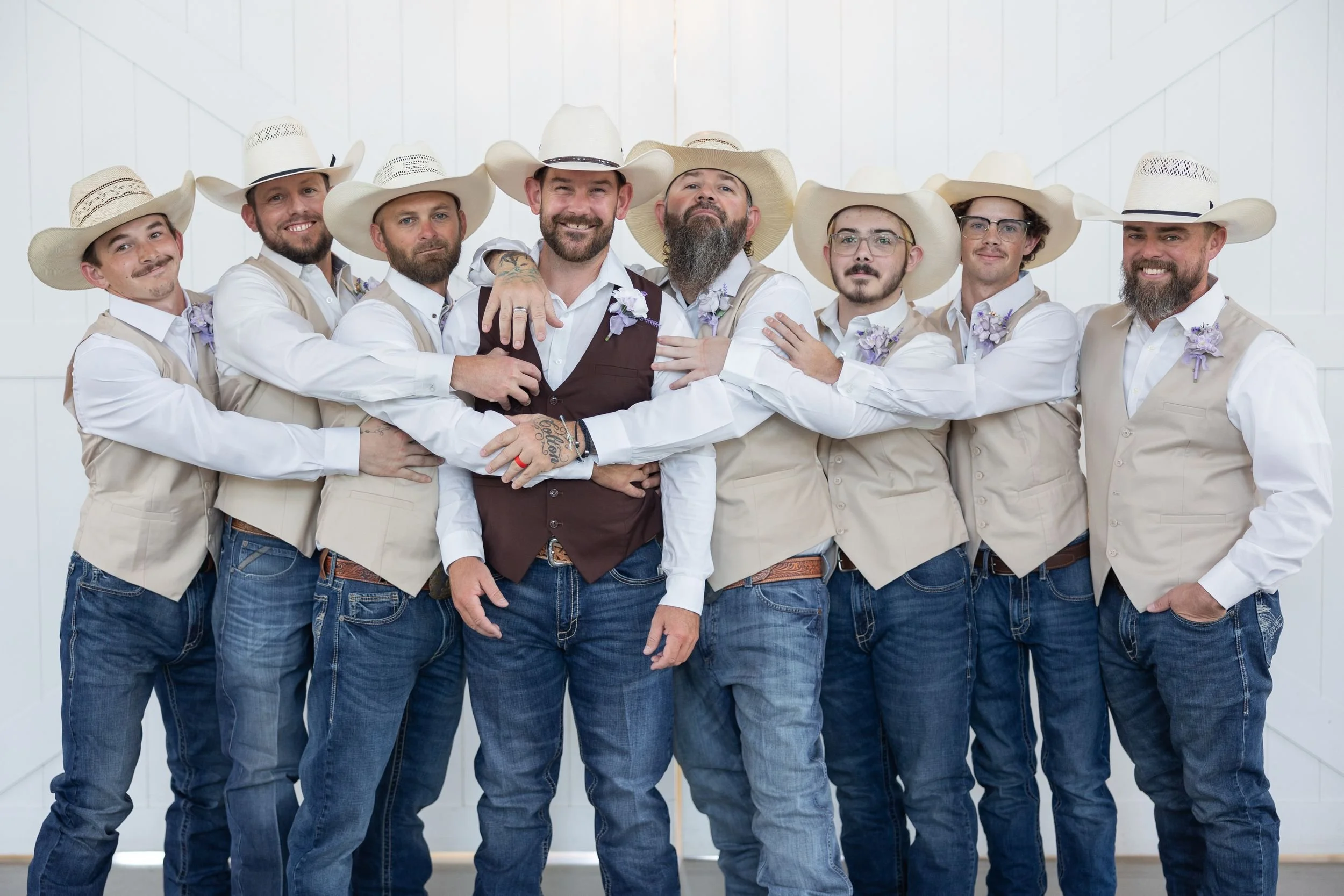 Groomsmen in cowboy hats and vests stacking hands before the ceremony