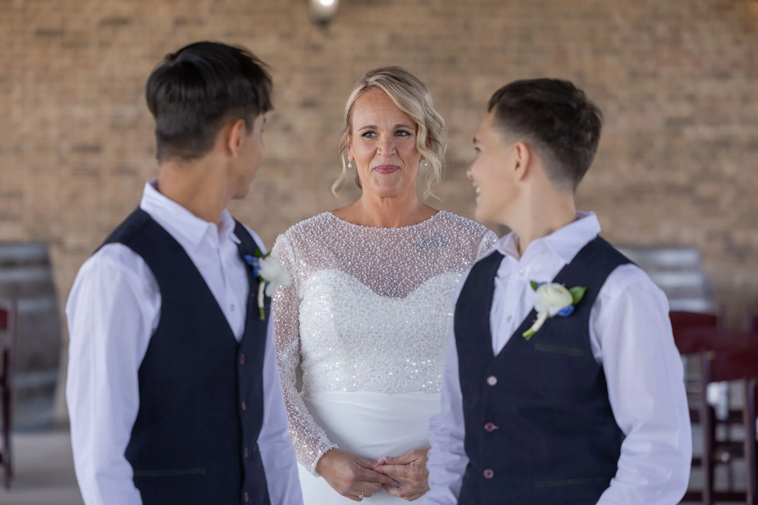 Bride laughing with two young groomsmen in navy vests before the ceremony