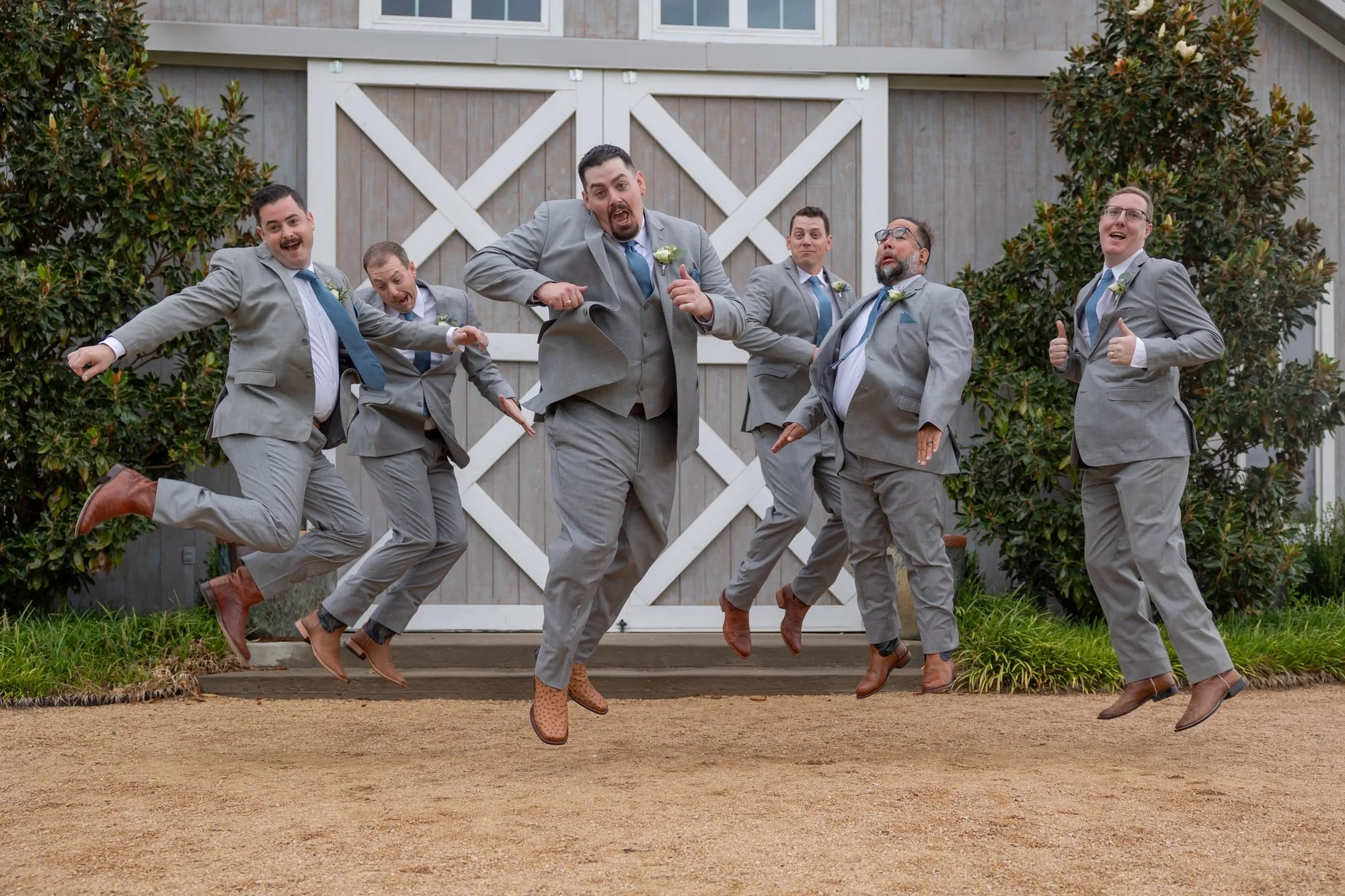 Groomsmen in gray suits jumping in front of a barn, a funny wedding party photo