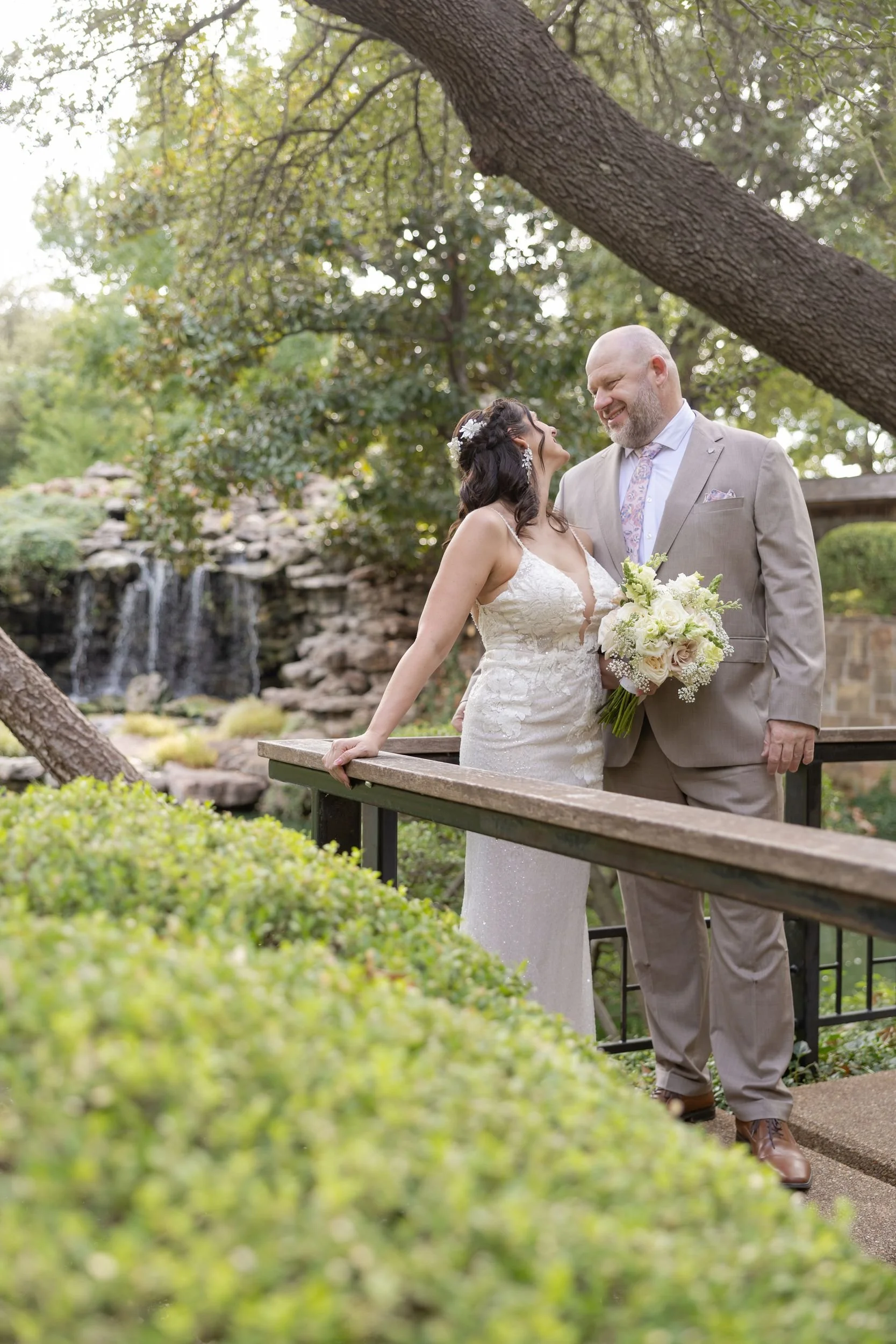 Couple embracing on a bridge surrounded by greenery, captured by Fort Worth wedding photographers