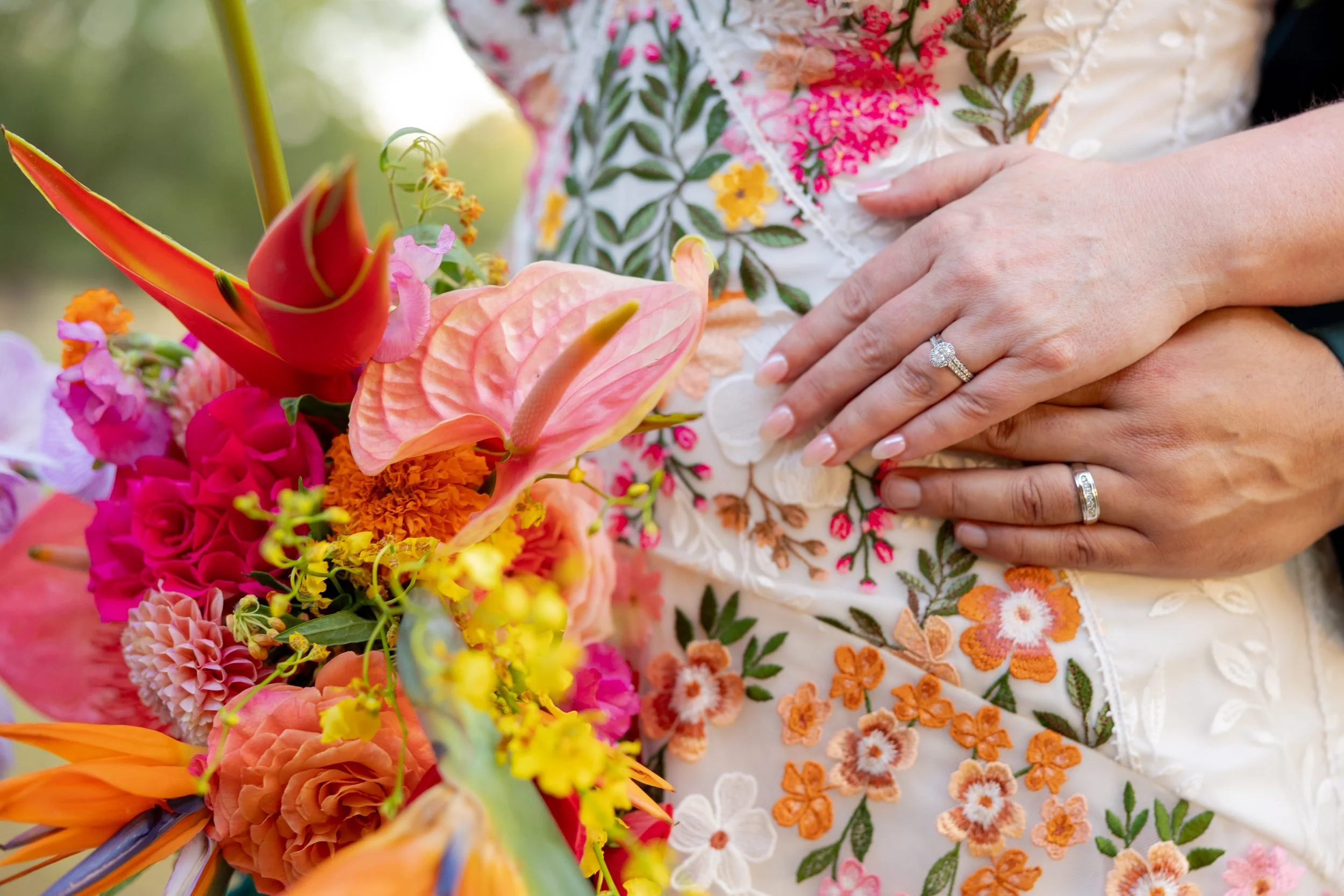 Bright tropical bouquet and wedding rings on the couple's hands