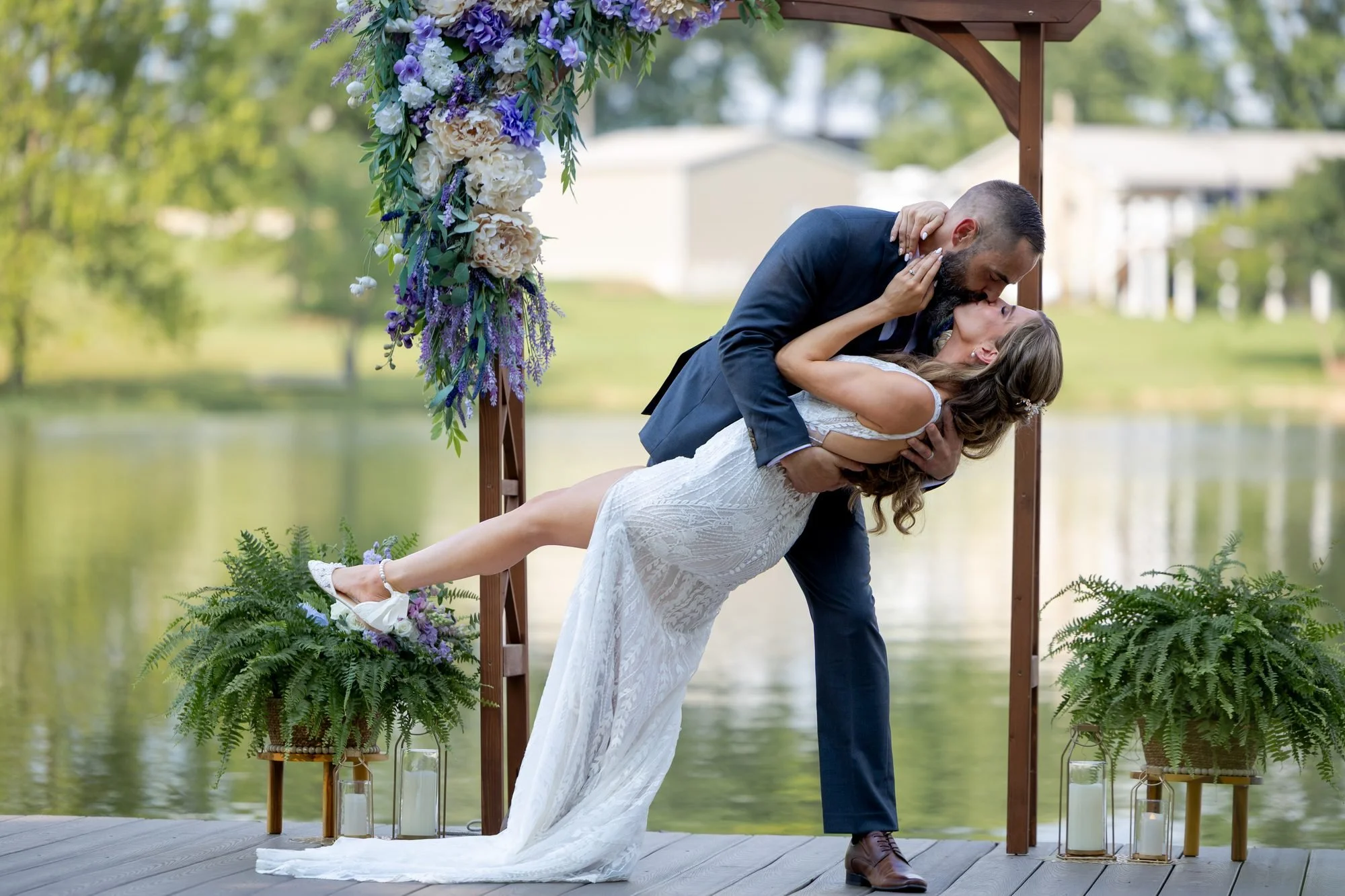 Groom dips the bride for a kiss under a floral arch at a lakeside Texas wedding ceremony