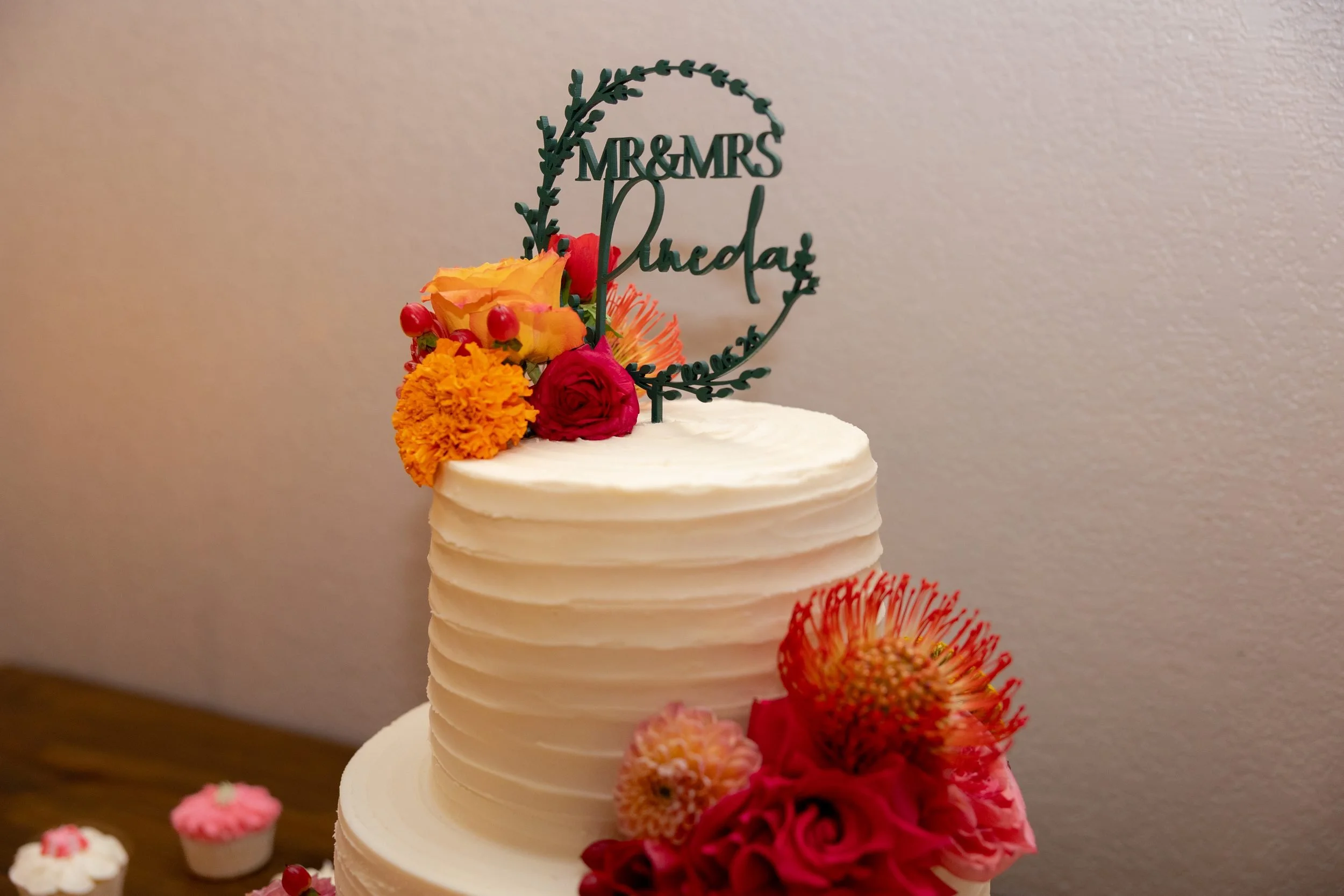 Wedding cake with a script topper and bright orange flowers at The Orchard reception