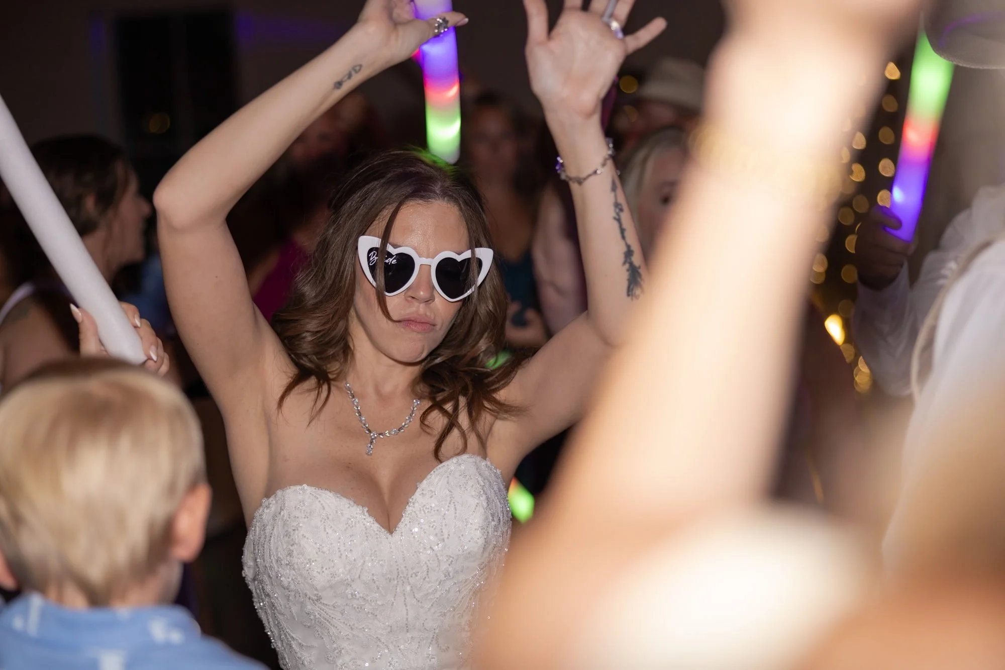Bride in heart-shaped sunglasses dancing with glow sticks at her wedding reception