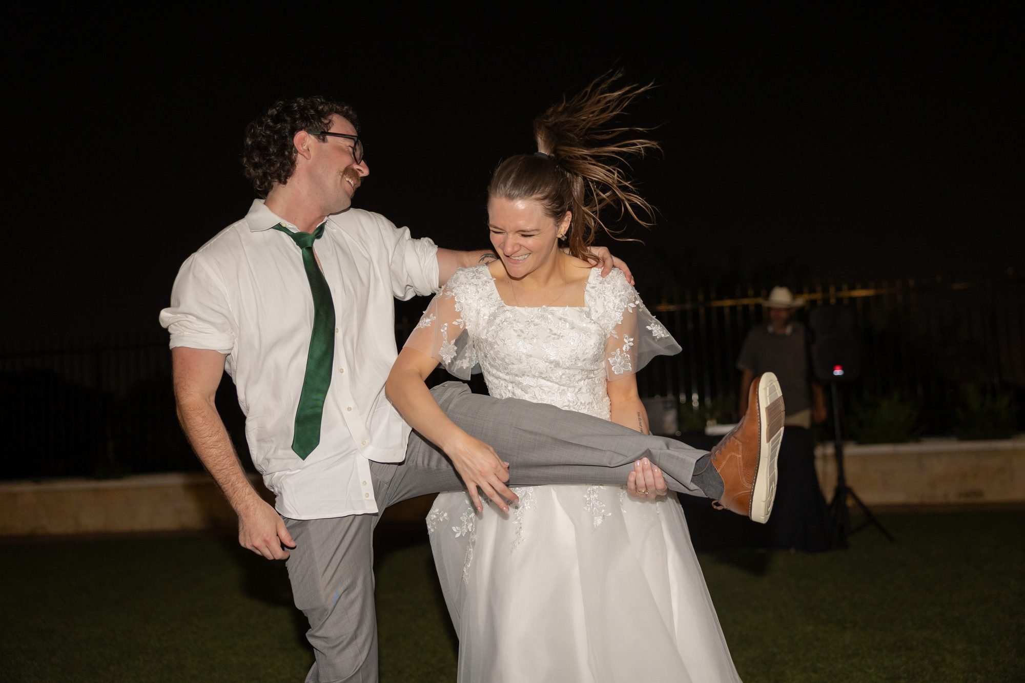 Funny wedding photo of a bride lifting the groom's legs during a nighttime dance move