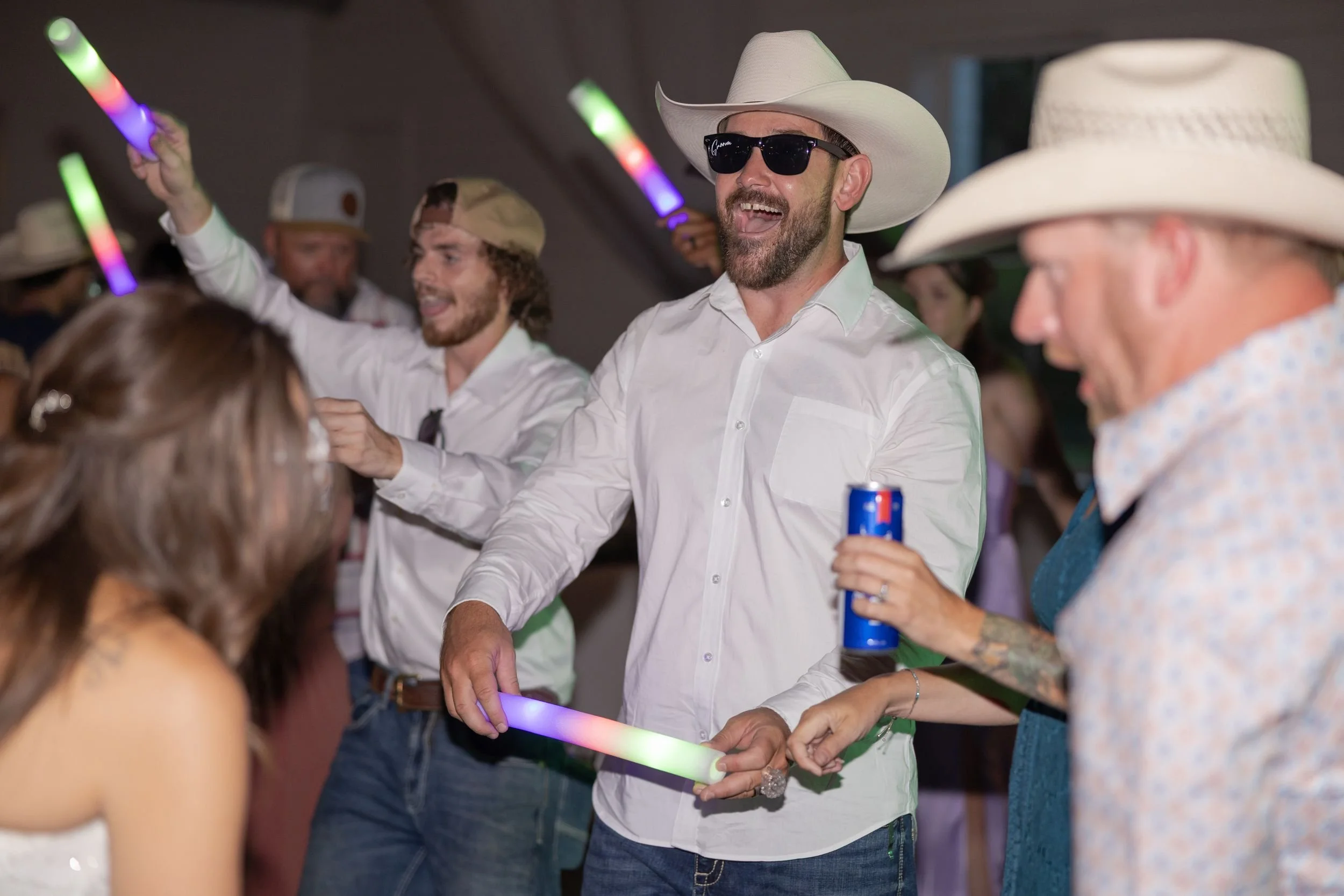 Groomsmen in cowboy hats celebrating with glow sticks during the send-off