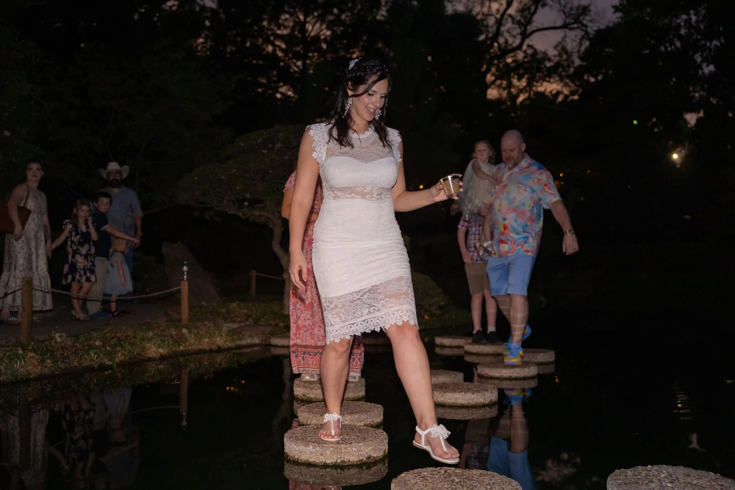 Bride and groom crossing stepping stones across the pond at night, Fort Worth wedding
