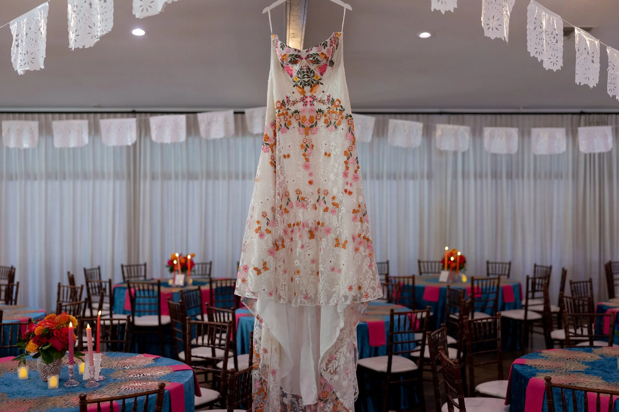 Carita's colorful floral wedding dress hanging in the reception hall at The Orchard