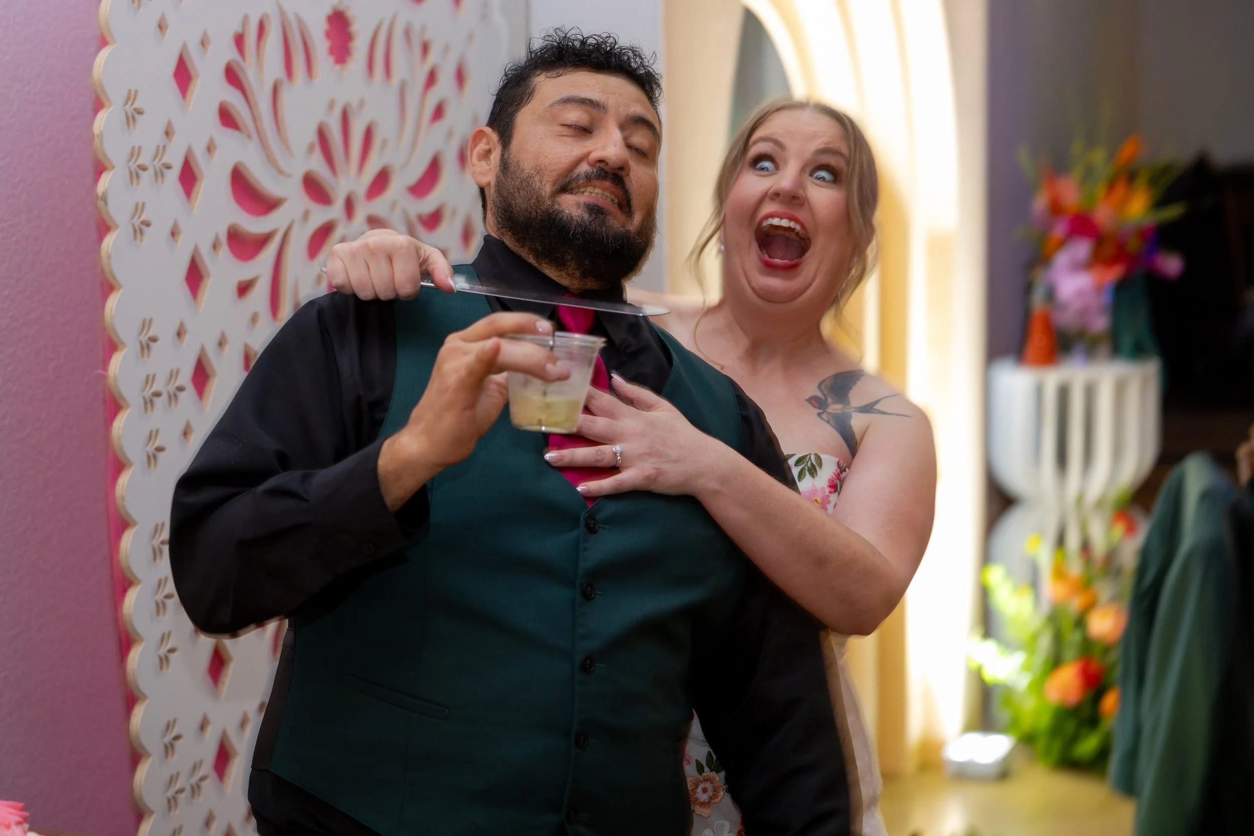 Carita and Miguel posing playfully in front of a papel picado backdrop at their reception