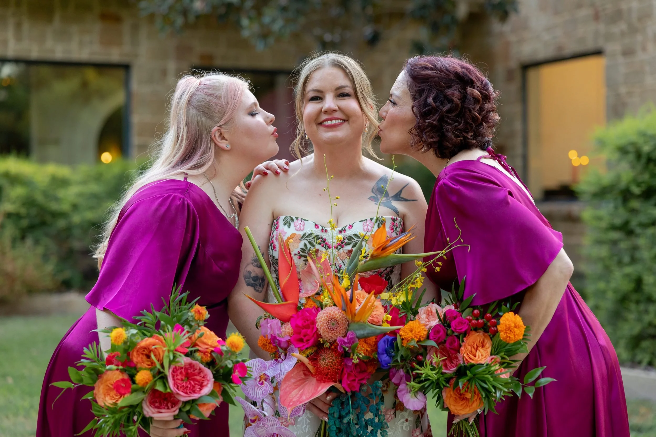 Bride laughing with her bridesmaids in magenta holding colorful bouquets