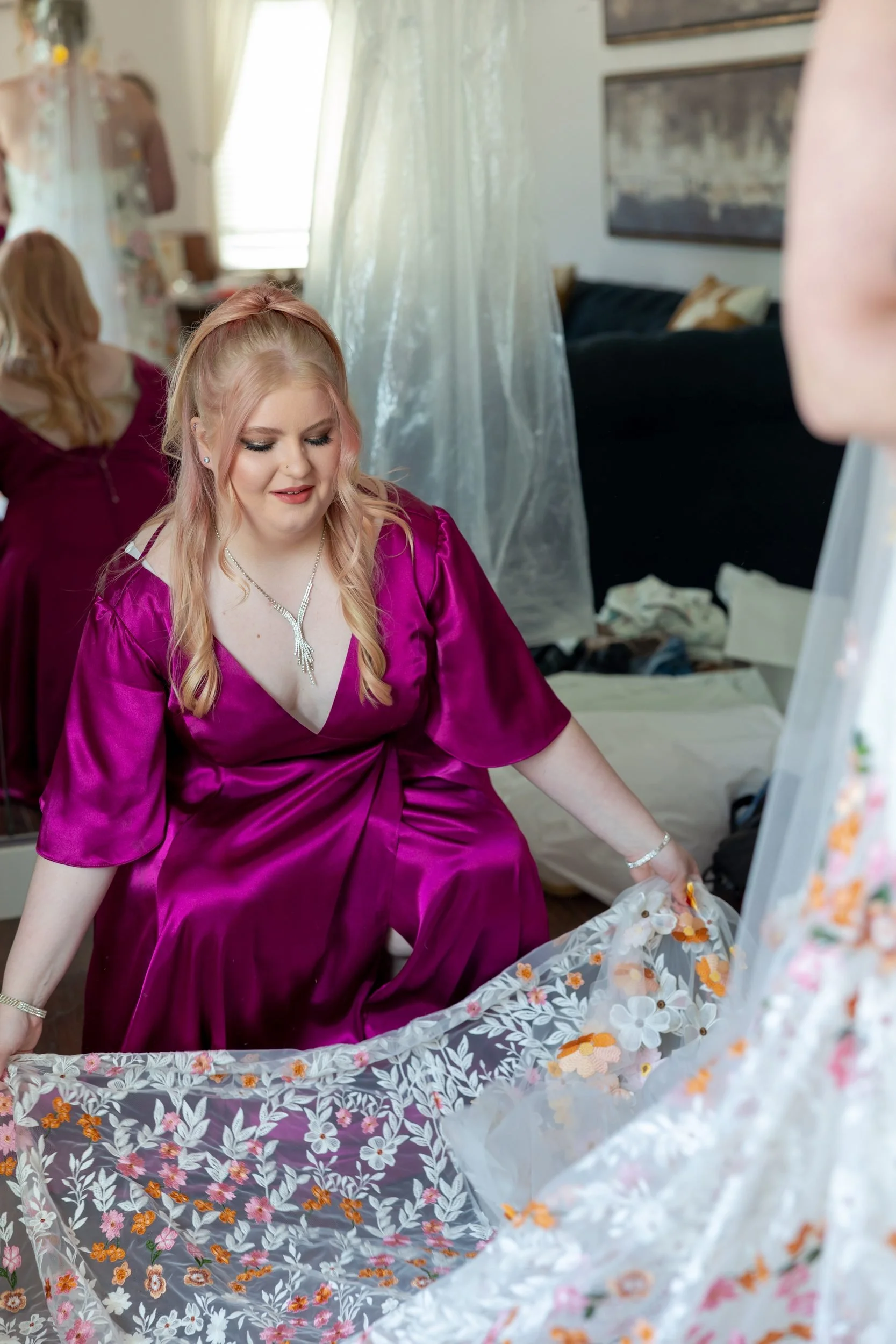 Bridesmaid in magenta helping the bride with her floral wedding dress