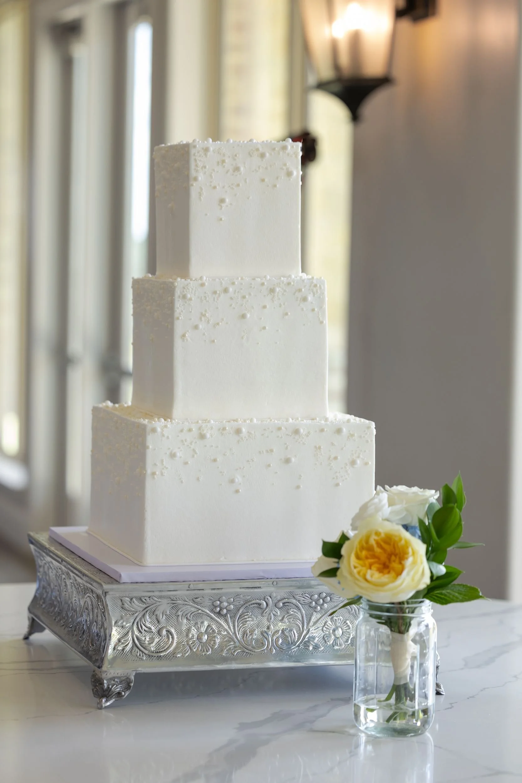 White tiered wedding cake with a yellow flower at the Dove Ridge Vineyard reception