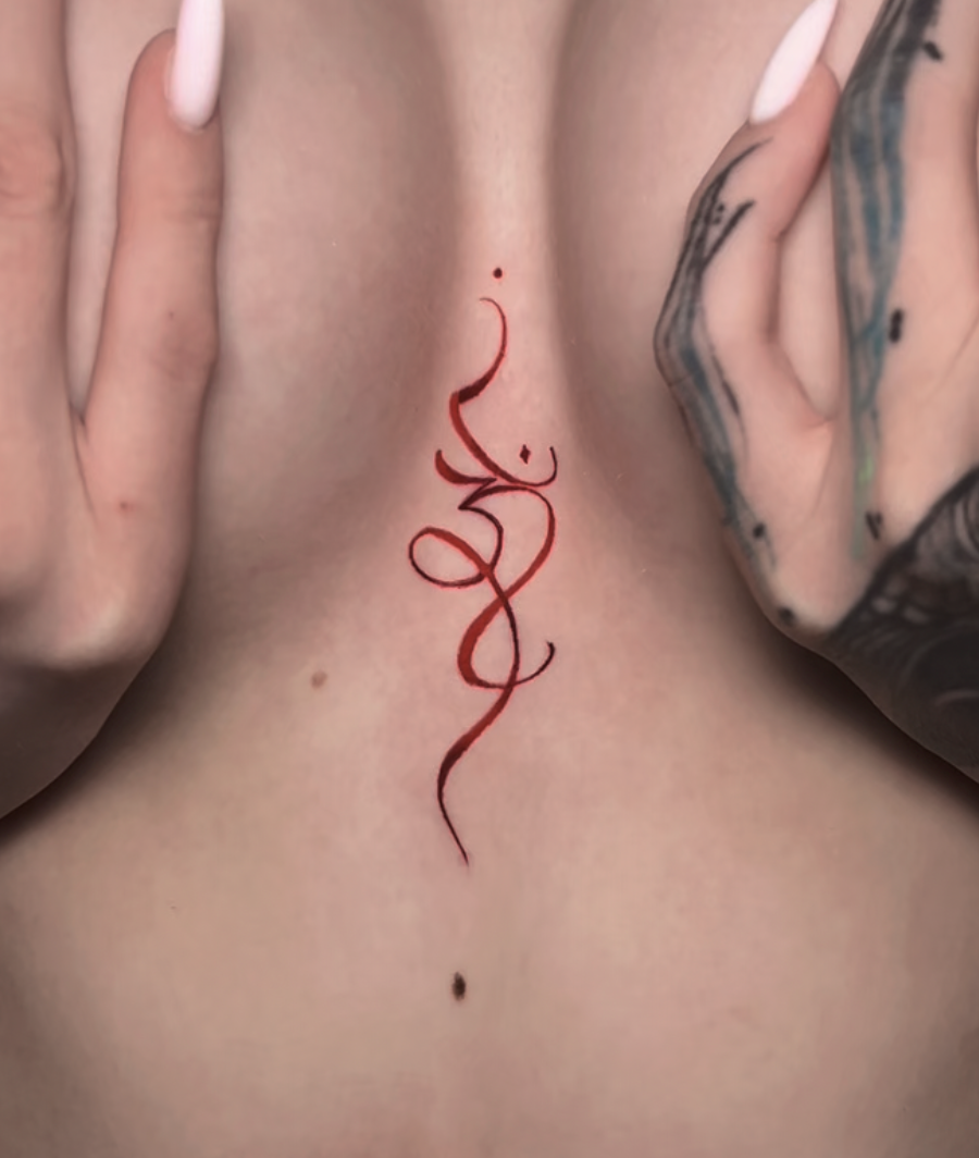 Red, stylized tattoo with swirling lines and small decorative dots, with hands framing the tattoo and visible tattoos on the fingers. Paris colored tattoo.
