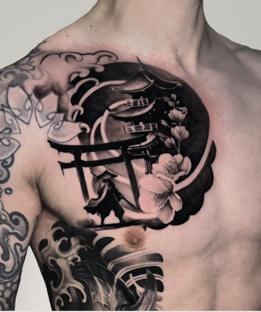 Tattoo on a person's chest featuring Japanese-inspired elements such as cherry blossoms, a torii gate, a pagoda, and traditional architecture, all rendered in black and gray ink.