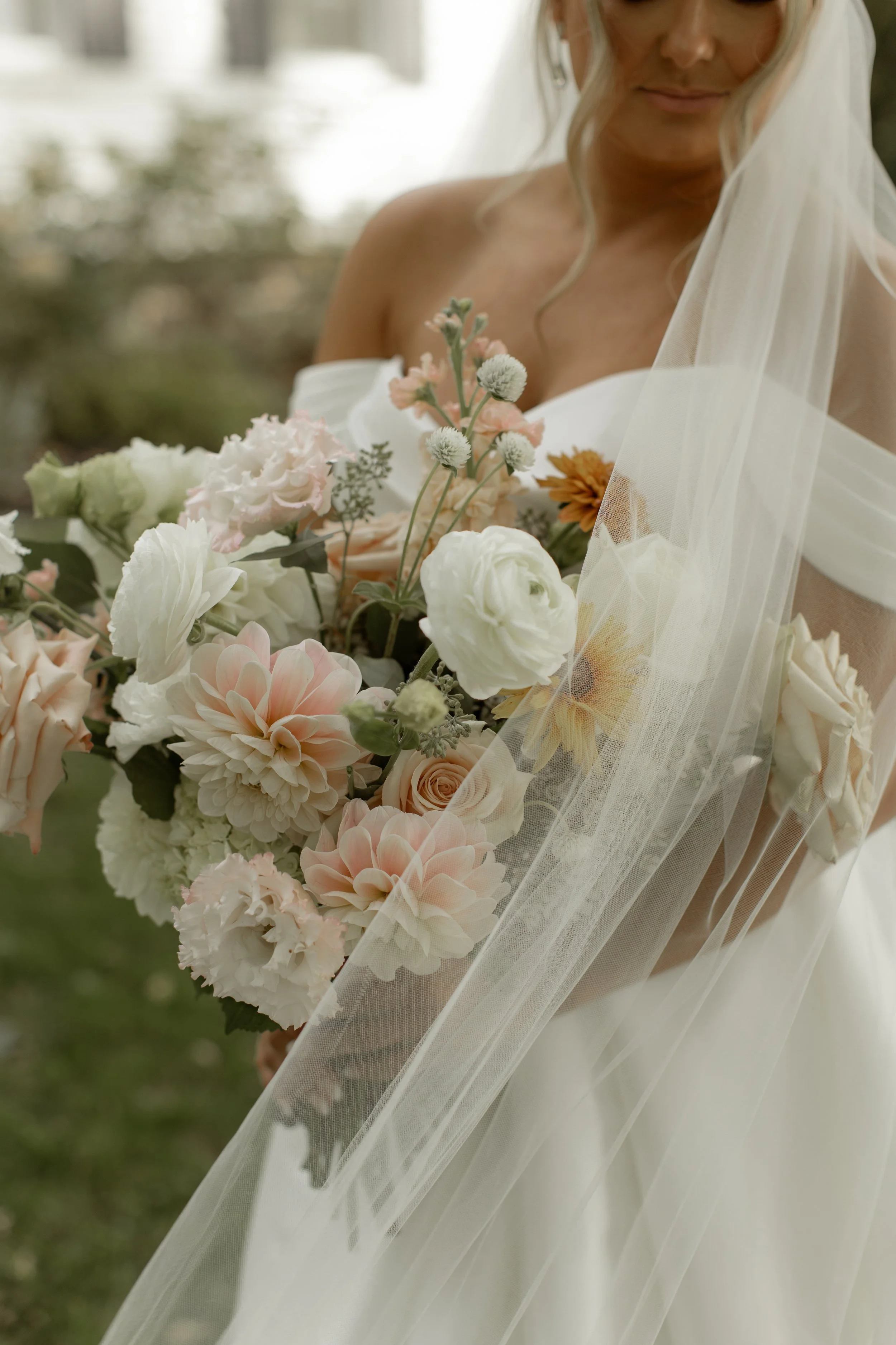 Close-up of a bride in a white veil holding a lush pastel wedding bouquet