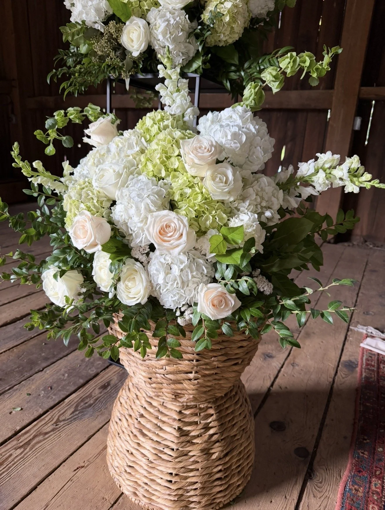 White and blush rose and hydrangea arrangement with greenery in a woven basket