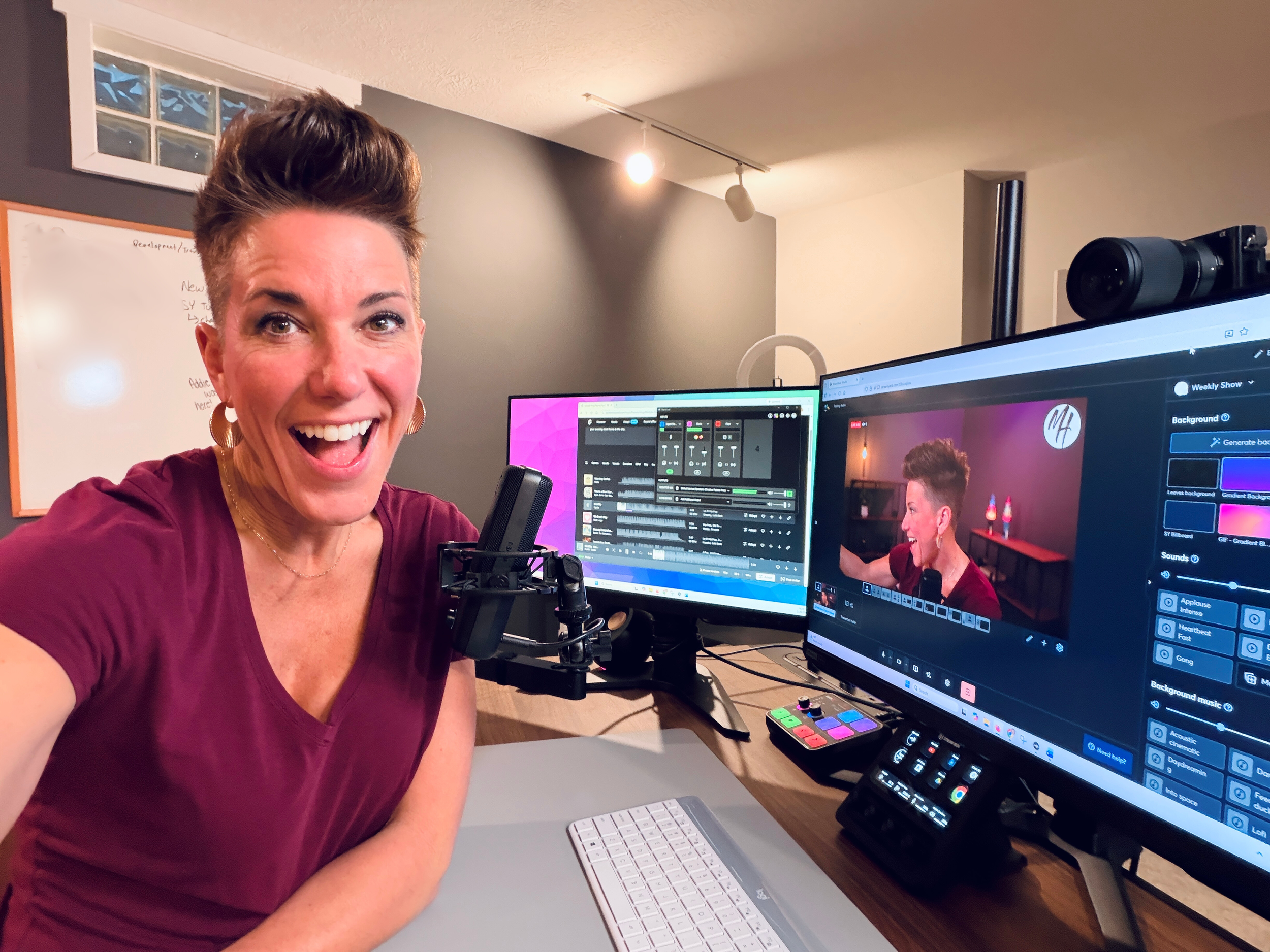 Mel at her livestream studio setup with monitors and a microphone. The room has two computer monitors displaying editing software, an Elgato microphone, and various electronic equipment on the desk.