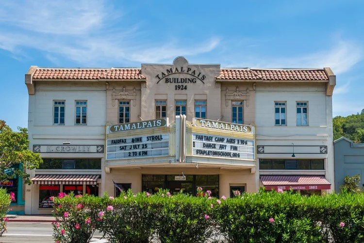 Front view of the Tamalpais Building, built in 1924, with a marquee announcing a fairy tale and dance event, and pink flowering bushes in the foreground.
