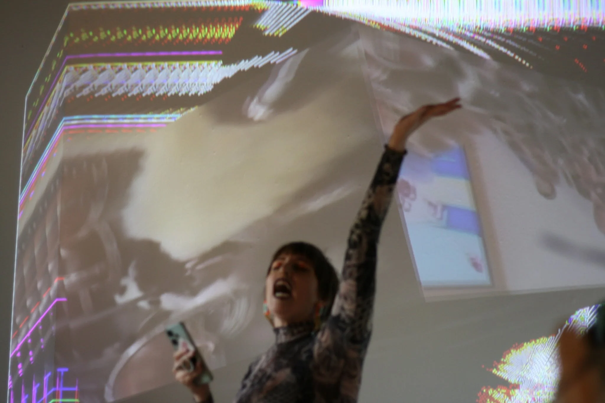 Person raising their arm holding a phone in front of a reflective, holographic-looking wall with colorful geometric patterns.
