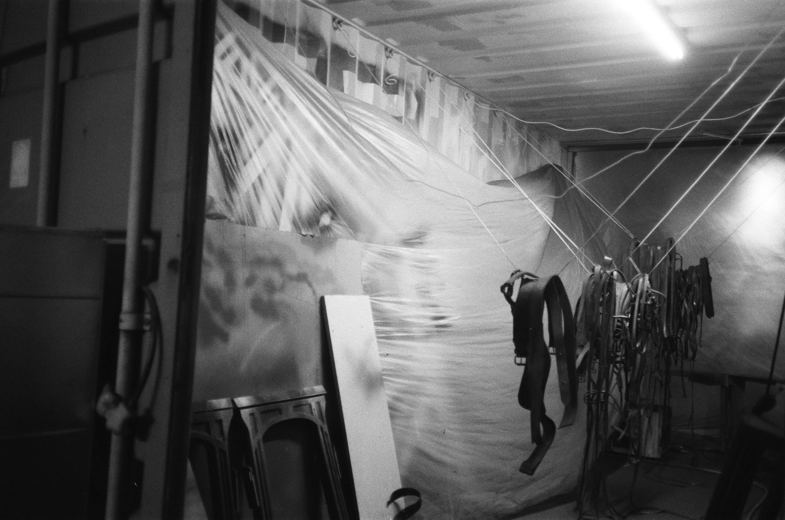 Black and white photo of a room with chairs stacked against the wall and various wires and cords hanging from the ceiling and scattered across the floor.