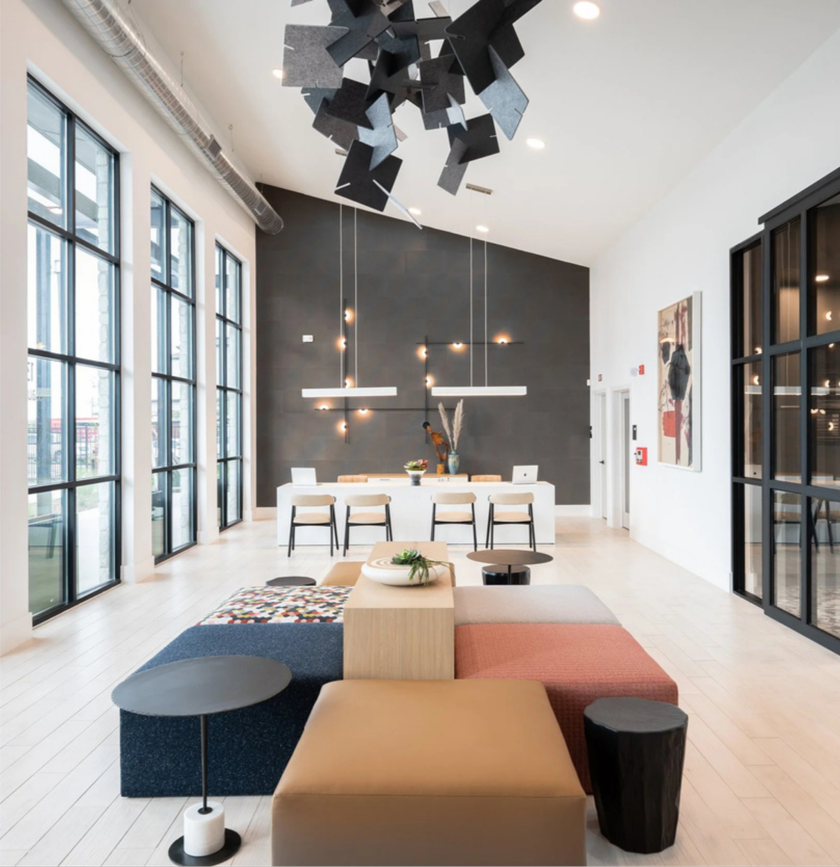 Modern lounge area with large windows, black and white furniture, and contemporary decor in a high-ceilinged space.