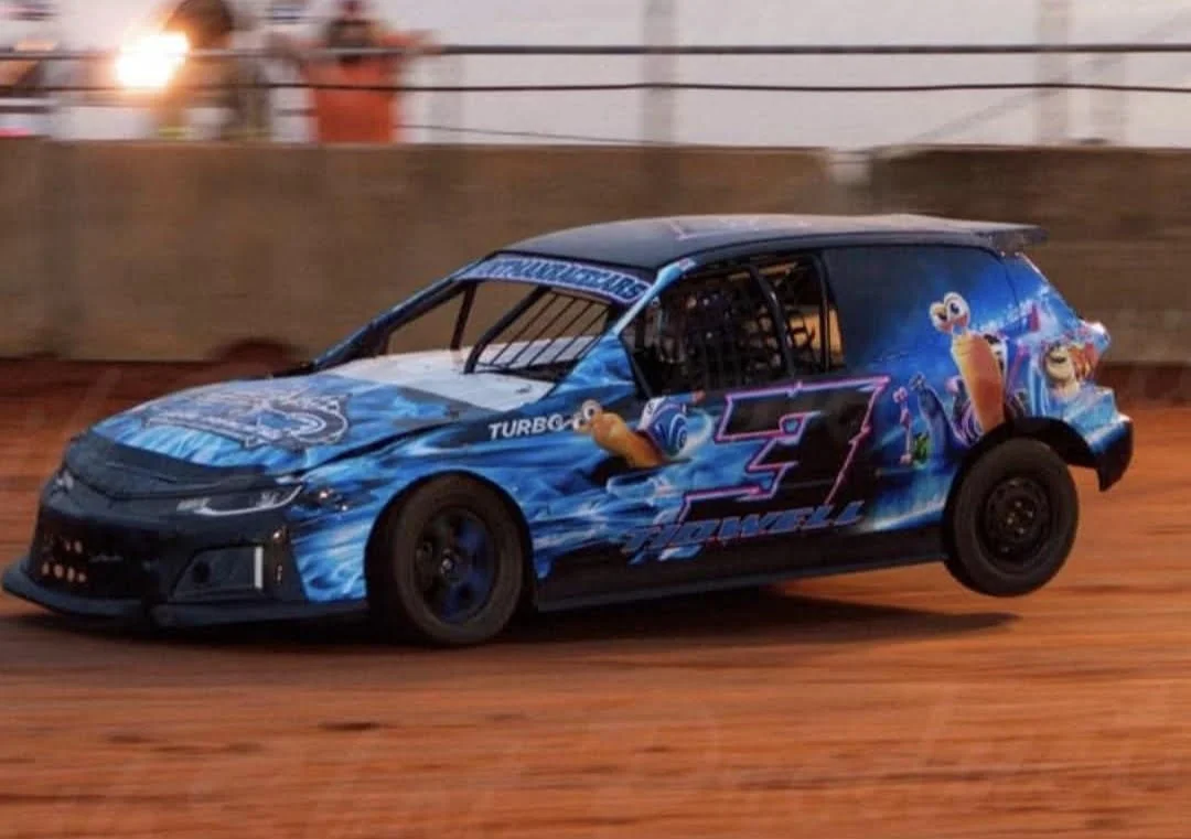 A race car with a blue and black design, featuring characters from Sesame Street, speeding on a dirt track.