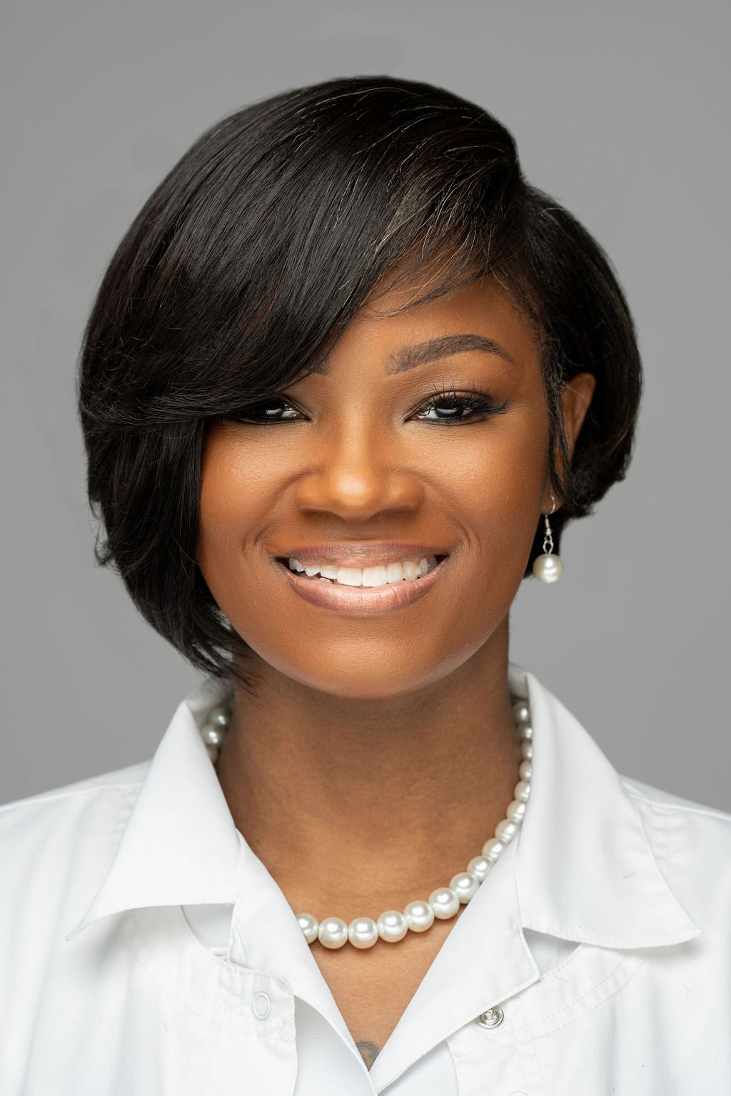 Founder and CEO of the home care organization, smiling in a white shirt with pearl jewelry against a gray background.