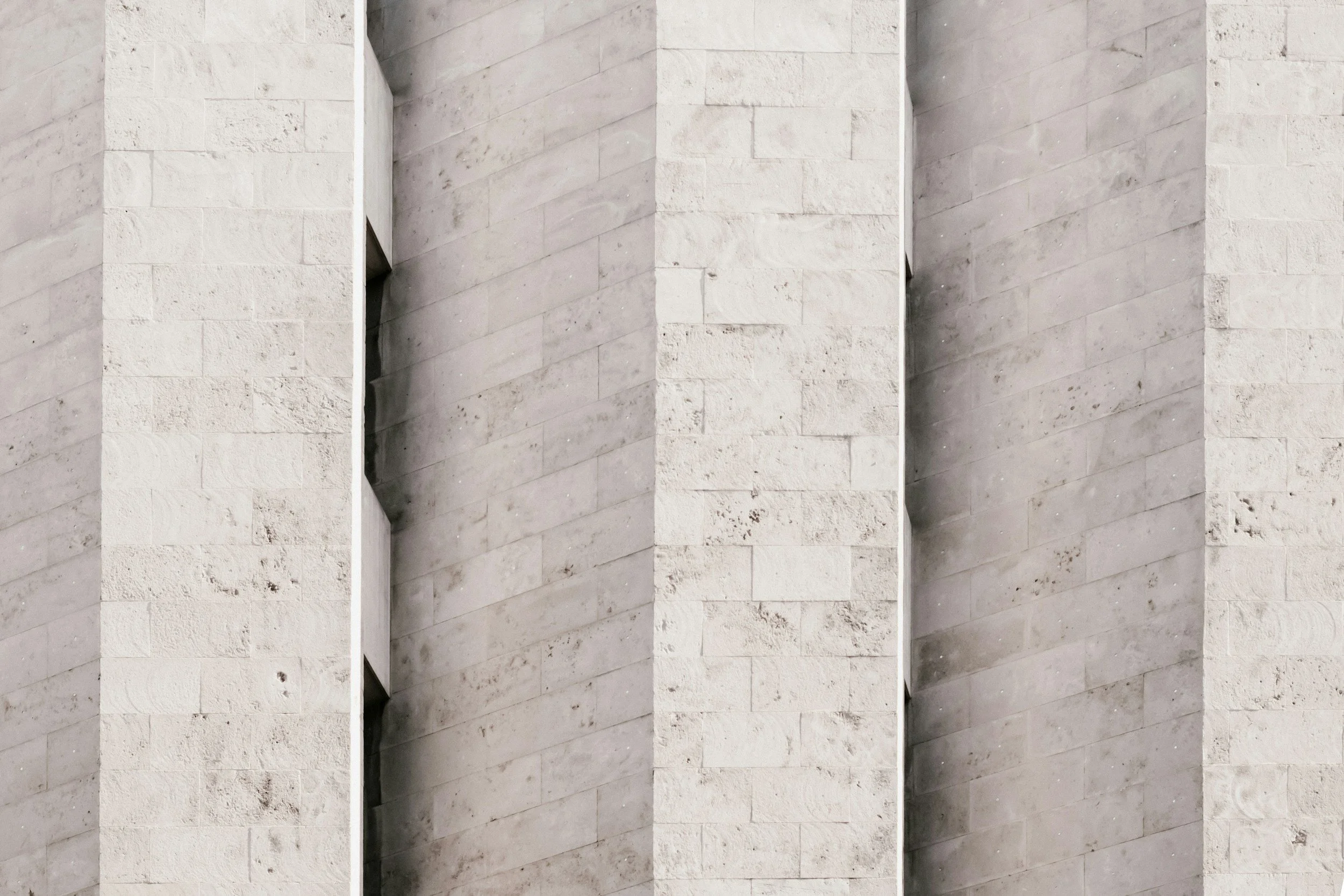 Close-up of a modern building's exterior wall made of light-colored stone bricks arranged in horizontal rows, with vertical corner joints.