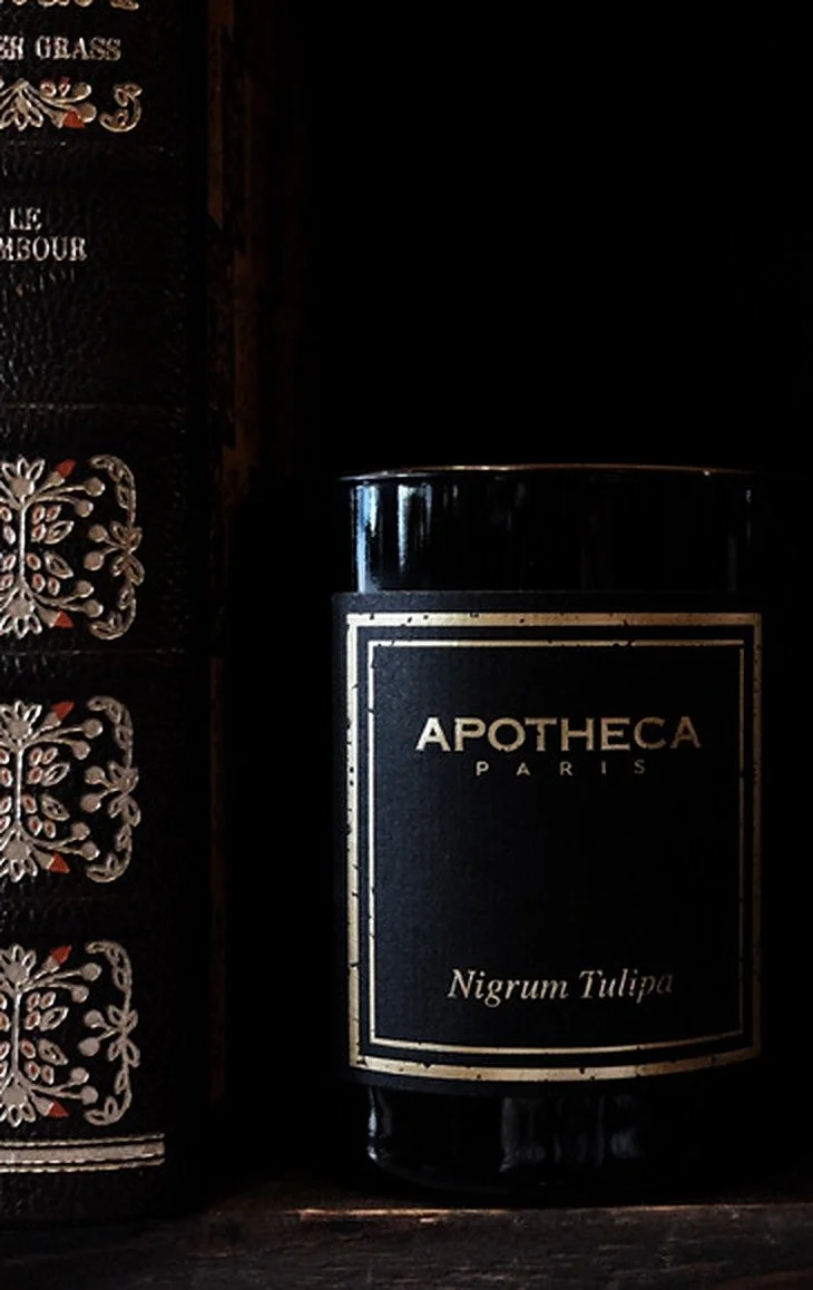 Apotheca Nigrum Tulipa candle on a shelf beside a gilt-tooled leather book