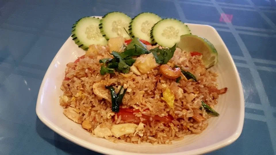 A bowl of fried rice garnished with cucumber slices, lemon, and cilantro.