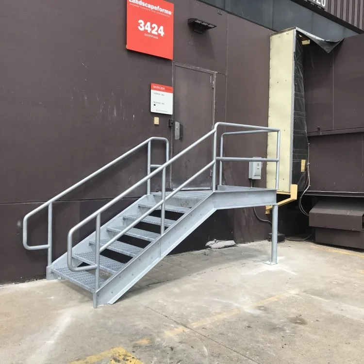 Custom metal outdoor staircase leading to a door on a dark building exterior, with a red signage above and a small signage near the door.