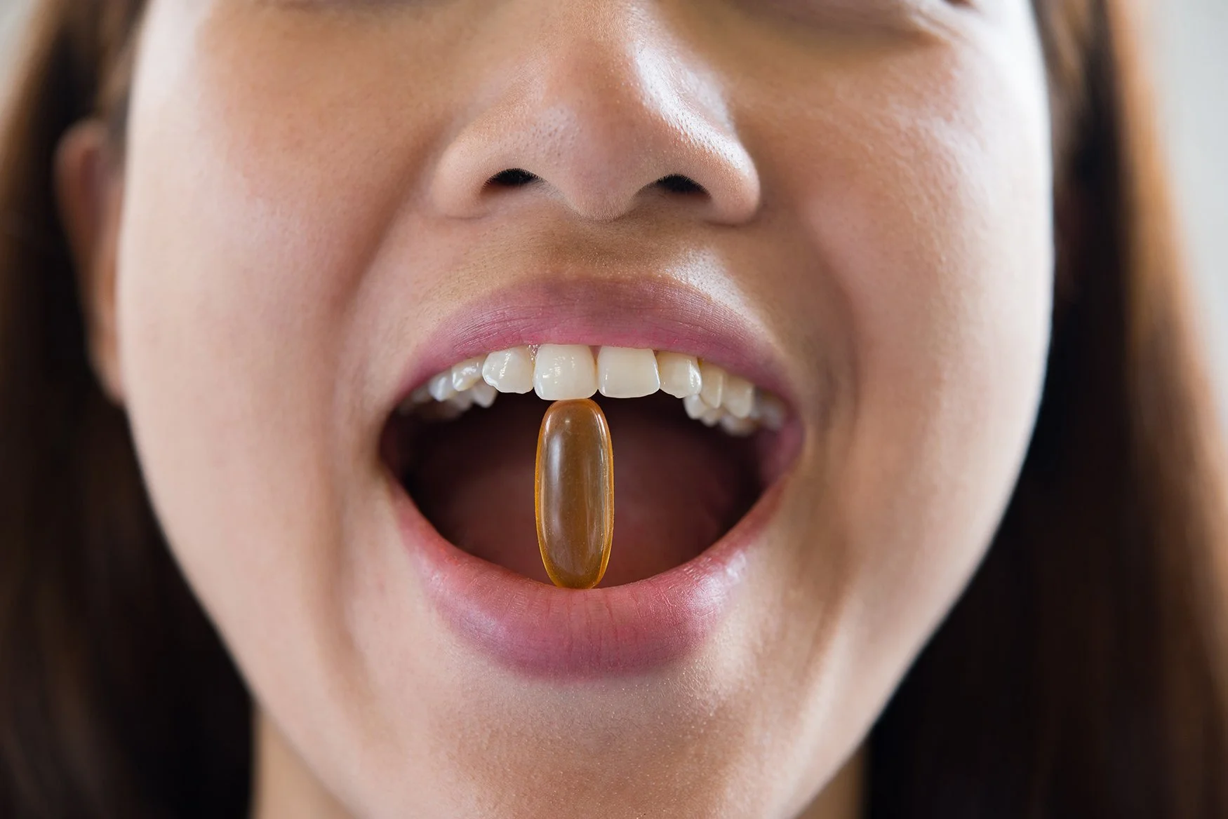 young woman holding gel cap supplement between her teeth