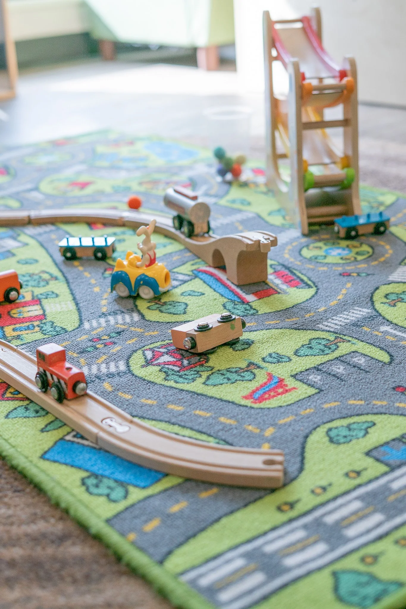 A colorful children's play rug with a train set and toy trains on it.