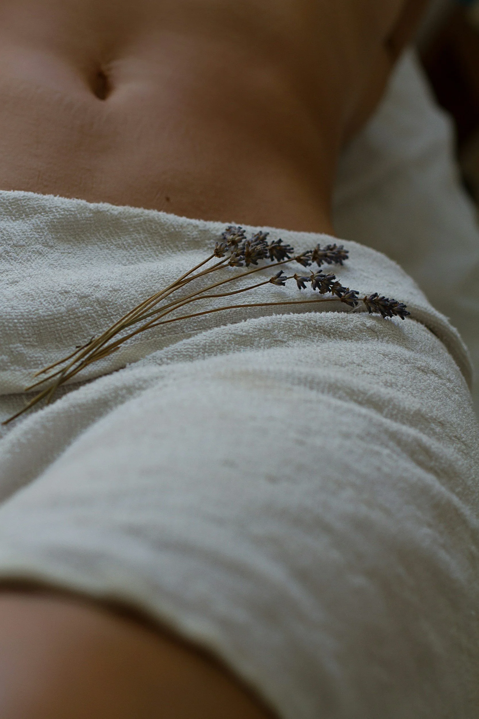 Close-up of a person's bare abdomen with a small lavender bouquet resting on white fabric.