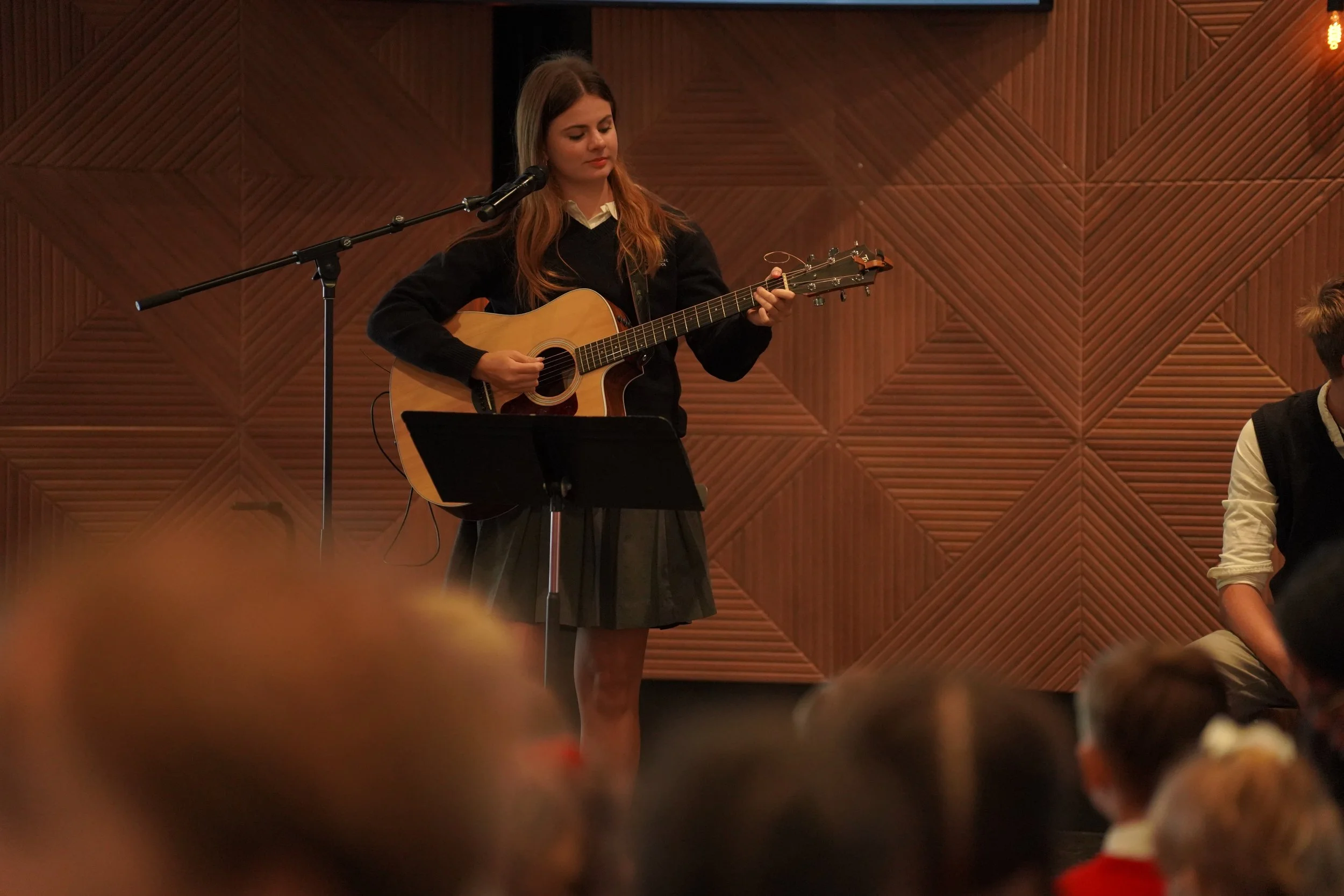Young woman singing into a microphone while playing acoustic guitar on stage before an audience