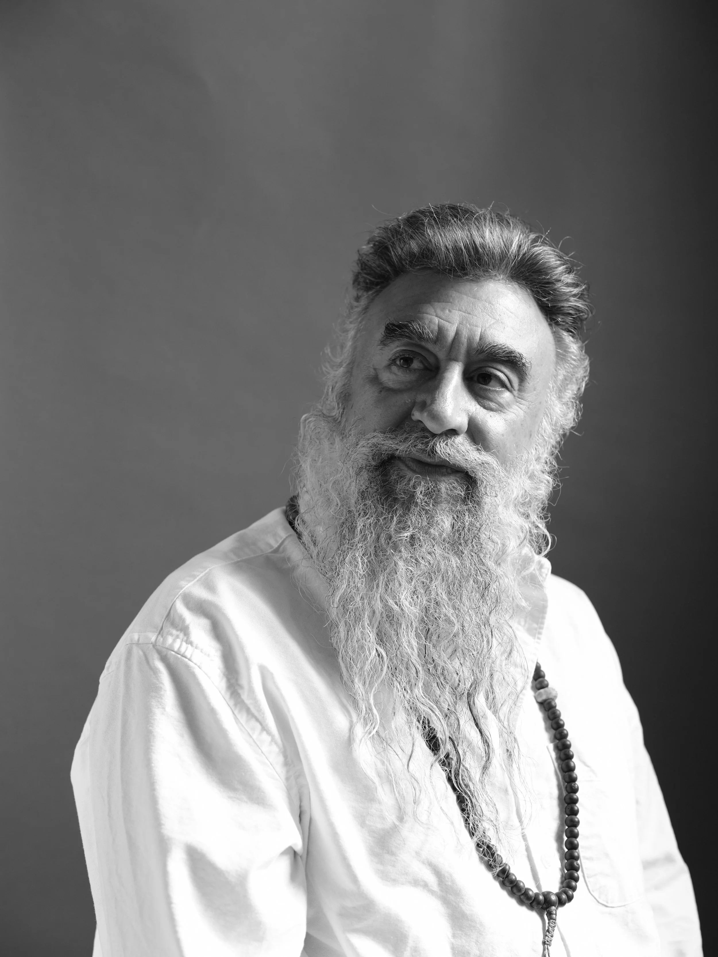 Retrato en blanco y negro de un hombre con barba larga, cabello arreglado y expresión reflexiva, llevando una camisa blanca y un collar de cuentas.