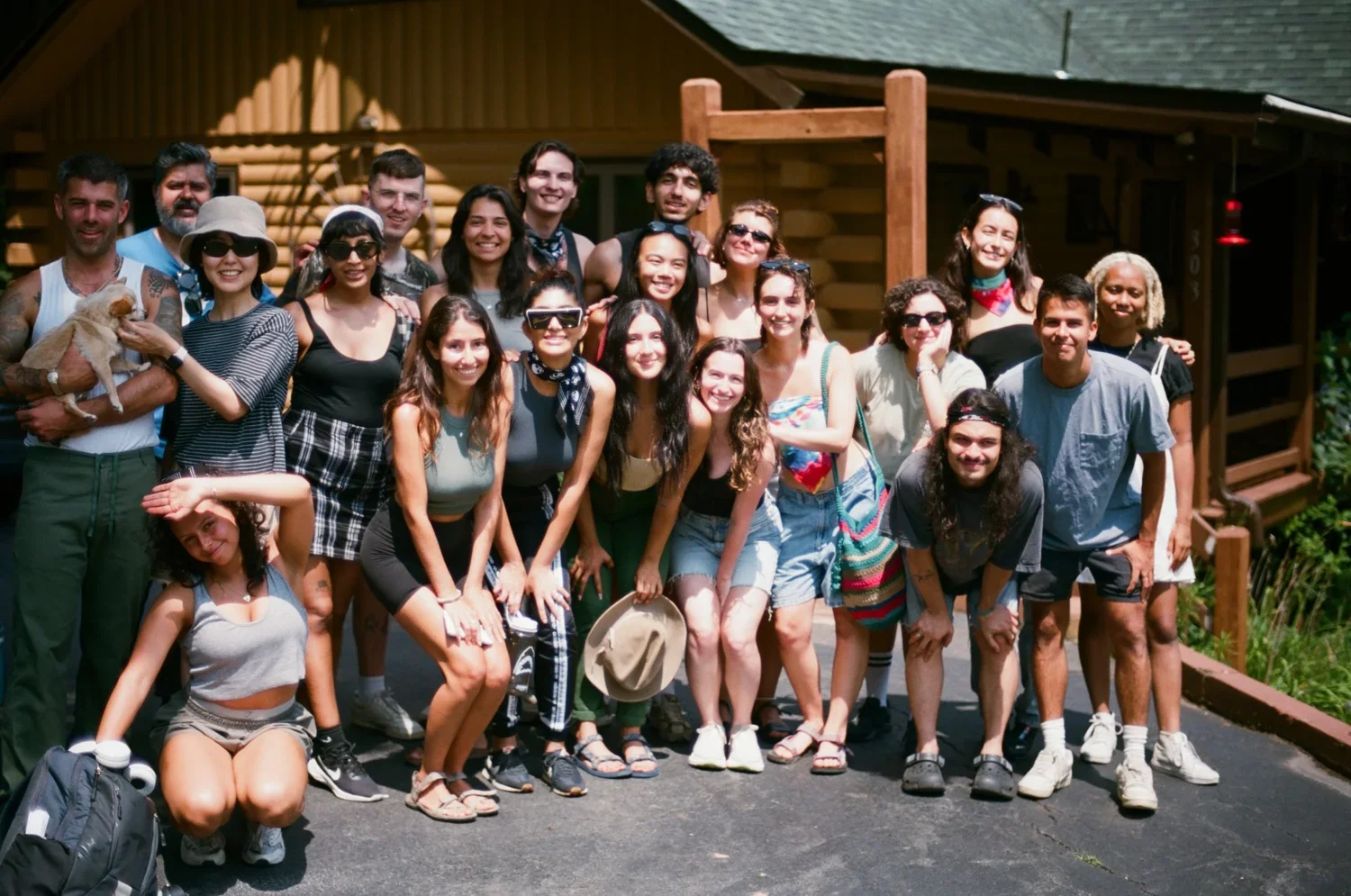 Grupo de personas sonrientes posando en un exterior en un día soleado, con una estructura de madera y casas al fondo.
