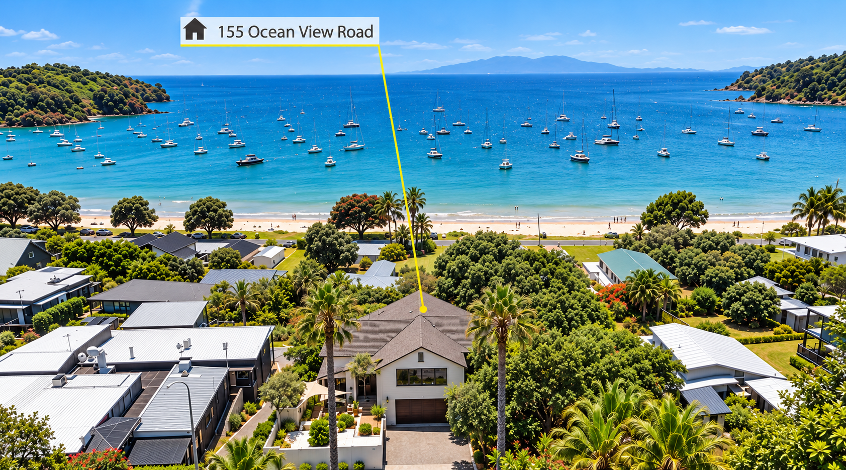 Aerial view of a coastal residential area with modern houses and lush green trees, facing a sandy beach with palm trees, and a harbor filled with sailboats and yachts in the ocean. A label points to a house on Ocean View Road.